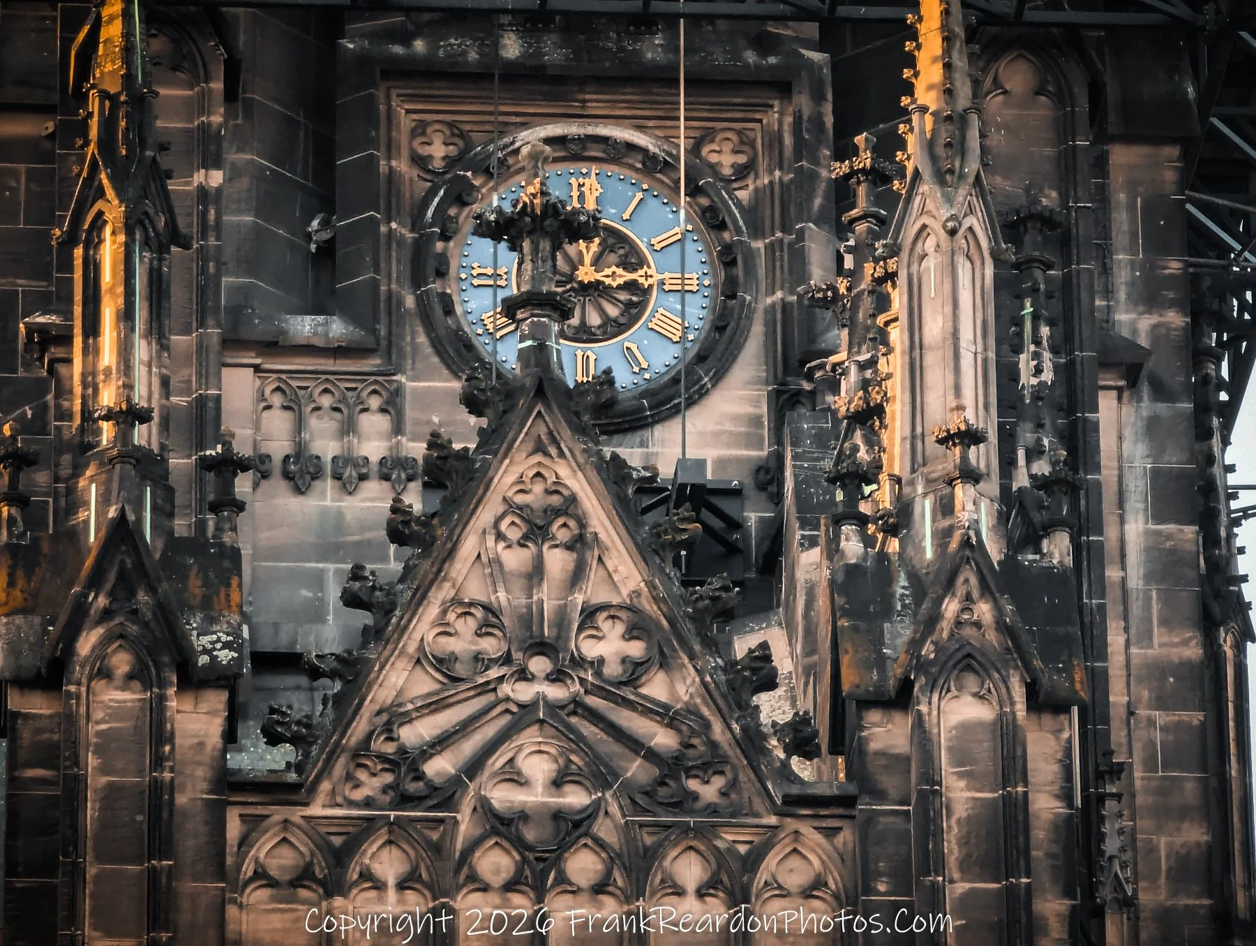 "Gothic Clock Tower Detail" A close-up of an ornate Gothic-style building, highlighting a blue clock face with gold Roman numerals and intricate stone masonry.