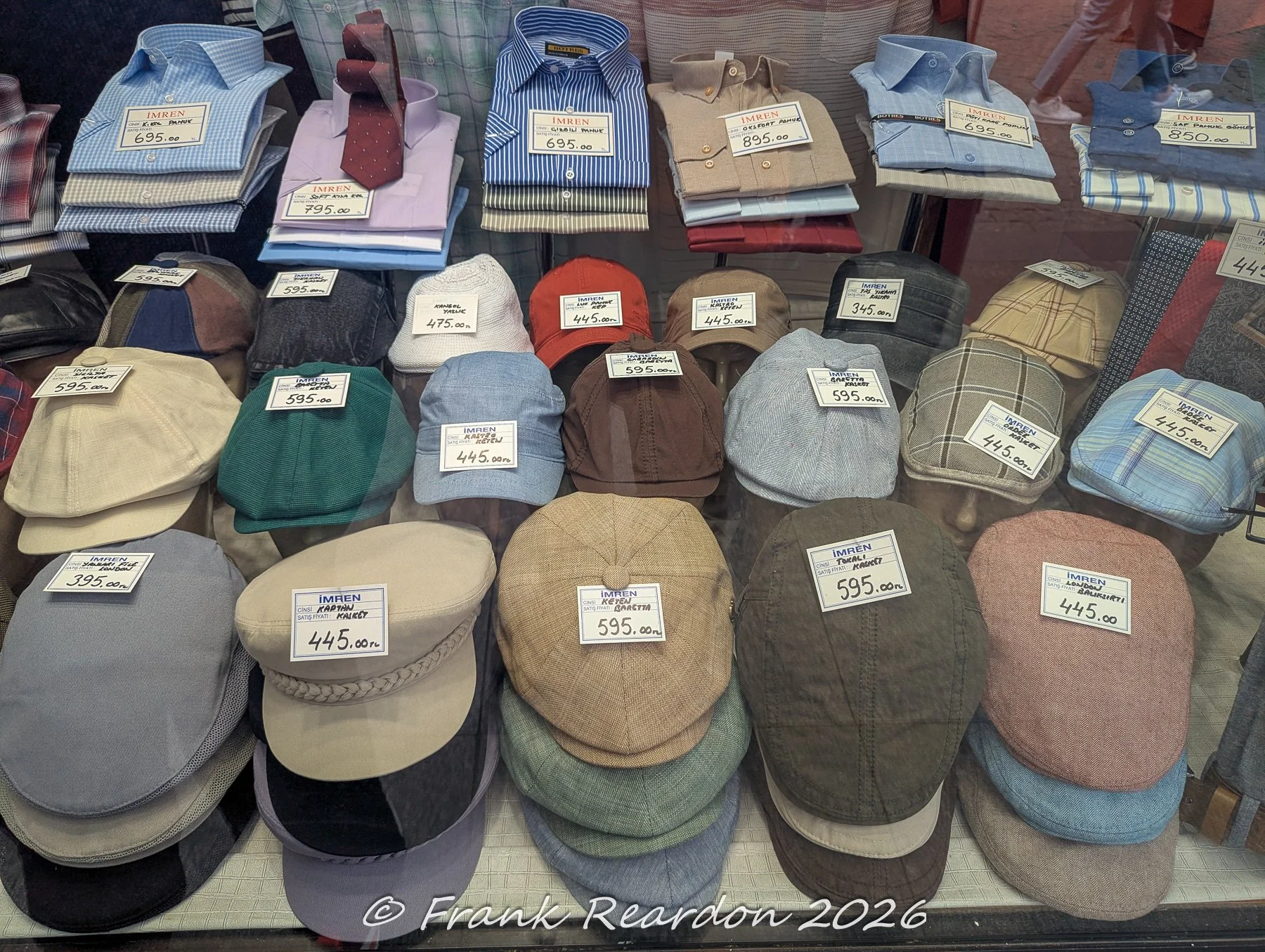 A market stall showcasing neatly stacked colored dress shirts alongside rows of tweed and fabric flat caps with price tags attached.