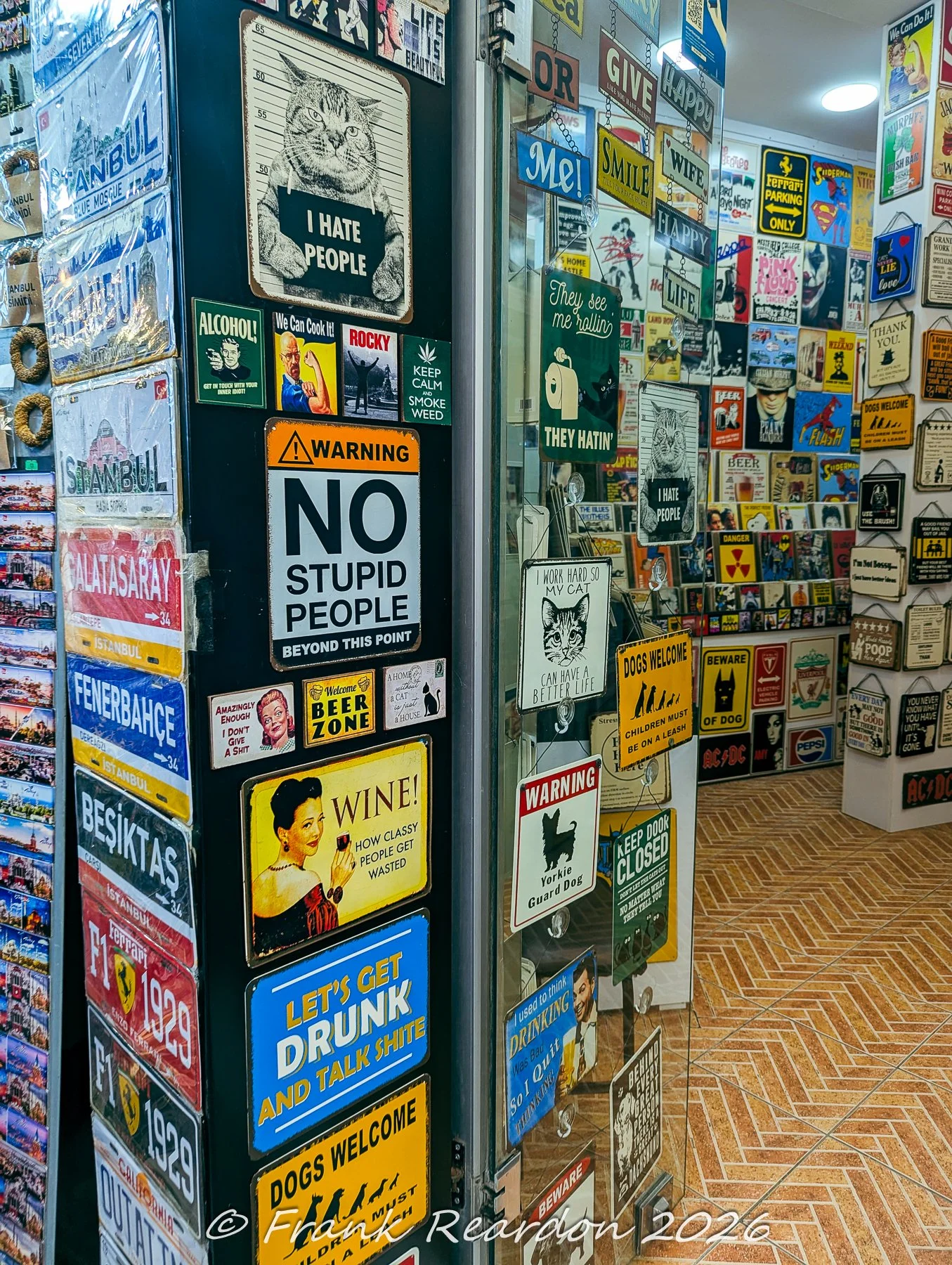 The entrance of a novelty gift shop densely covered with humorous, pop-culture, and football team tin signs.