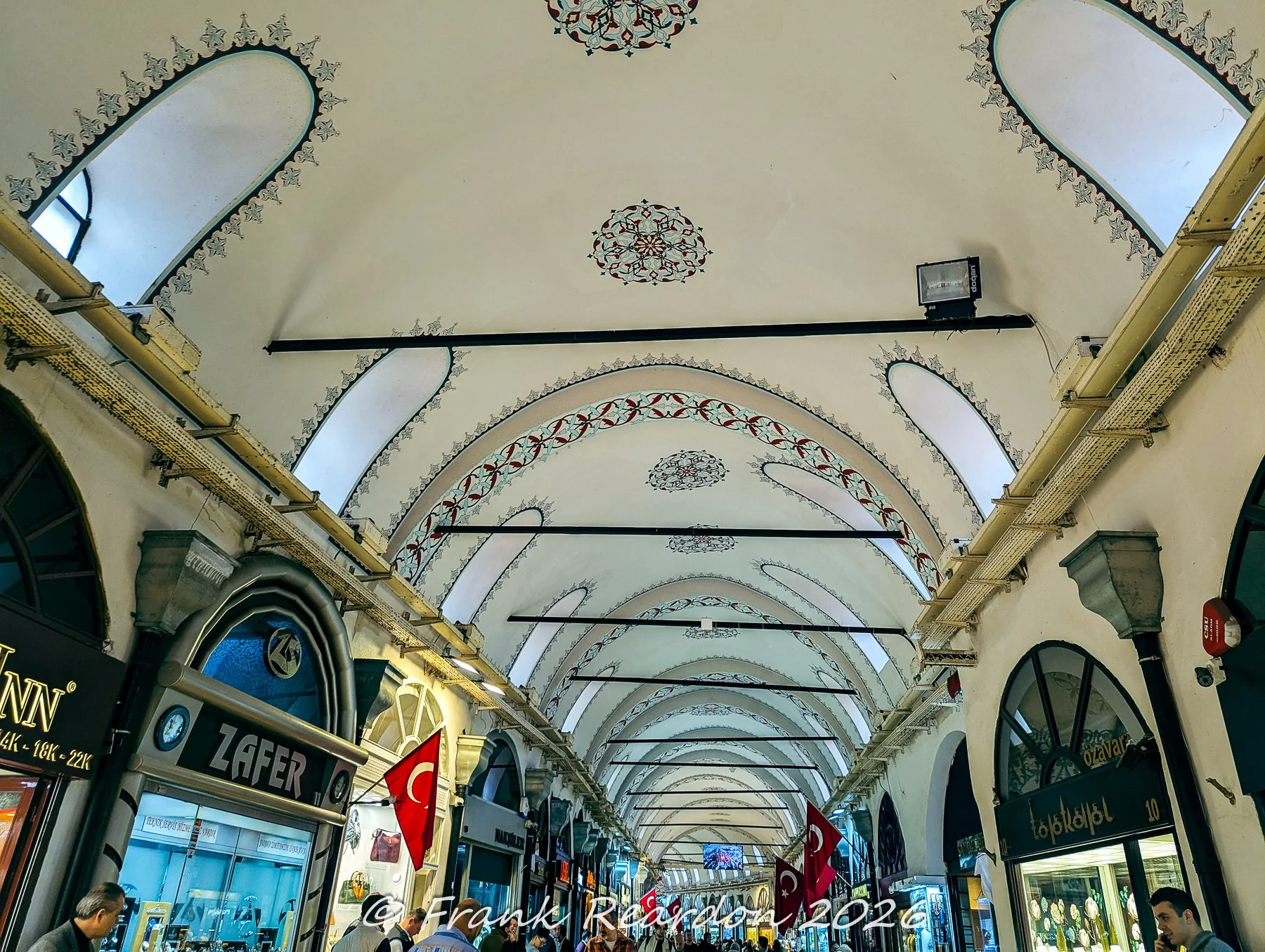 A perspective looking up at the whitewashed, arched ceilings and decorative painted borders spanning the interior corridors of the Grand Bazaar.