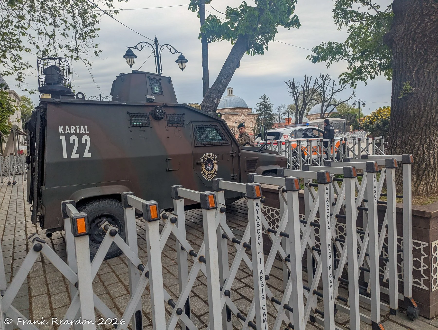 An armored security vehicle parked near metal security barriers and officers on a city street in Istanbul.