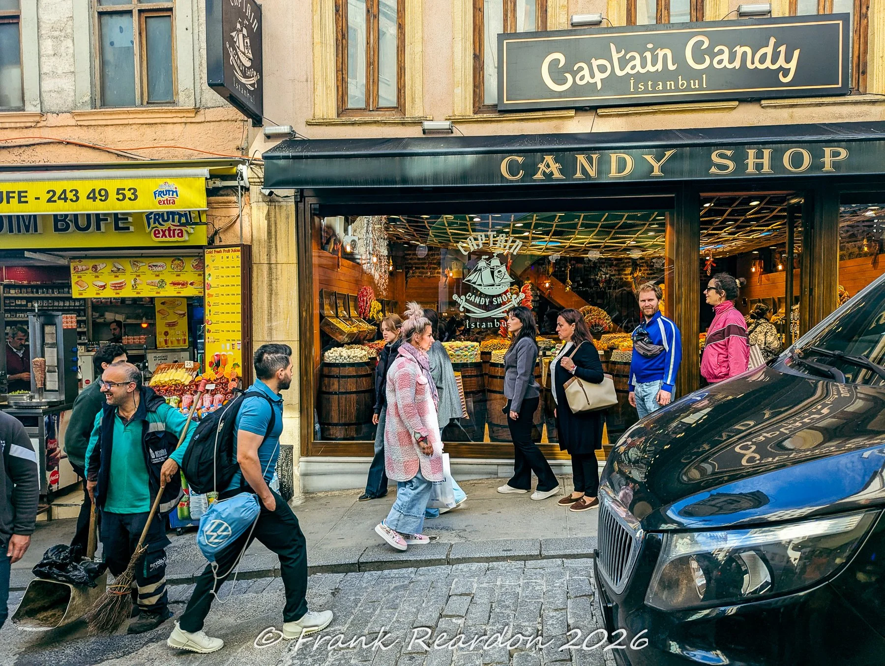 A lively street view featuring the storefront of Captain Candy Istanbul with pedestrians, a nearby snack buffet, and street life.