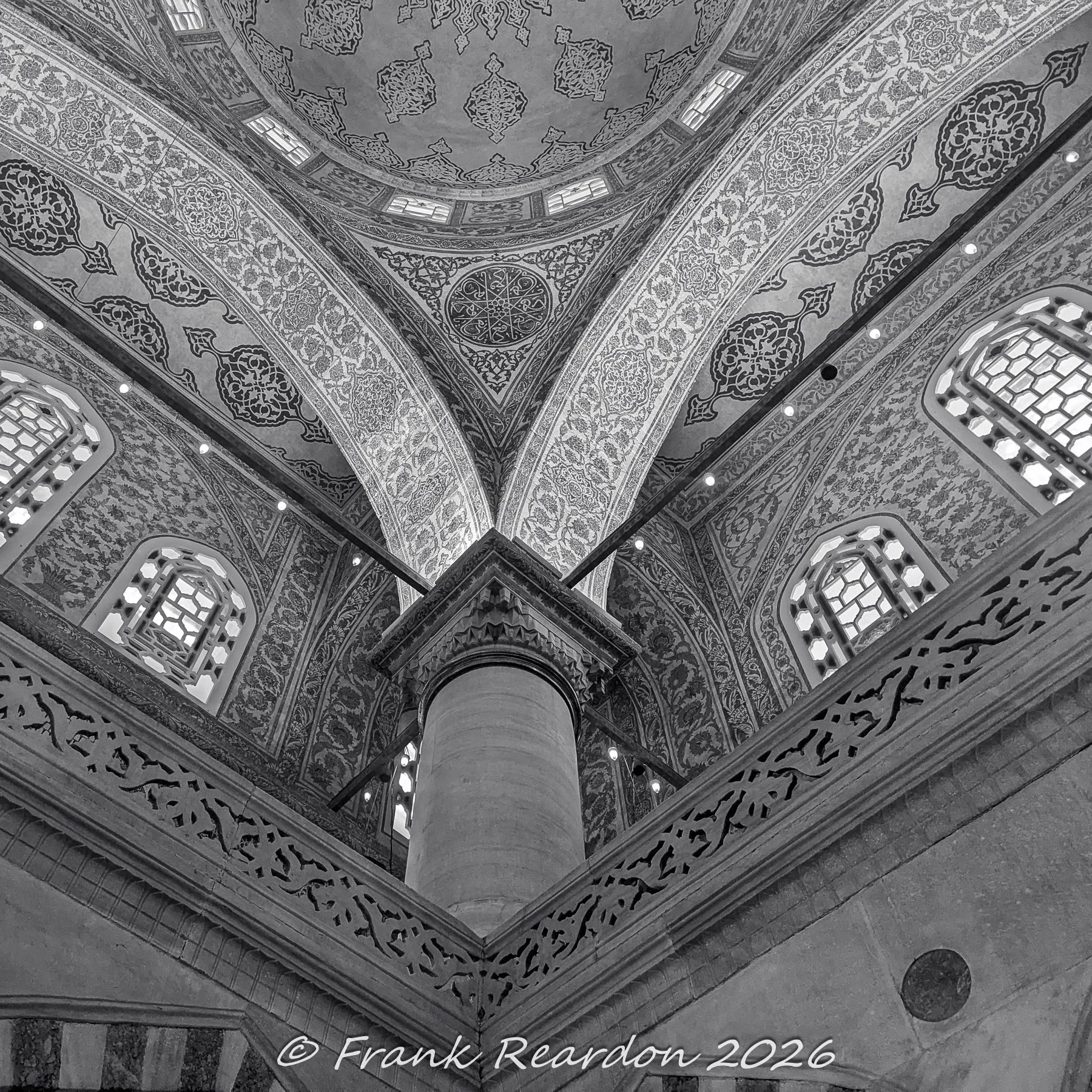 A monochrome, detailed look upward at one of the massive central columns, vaulted arches, and windows inside the Sultan Ahmed Mosque (Blue Mosque).