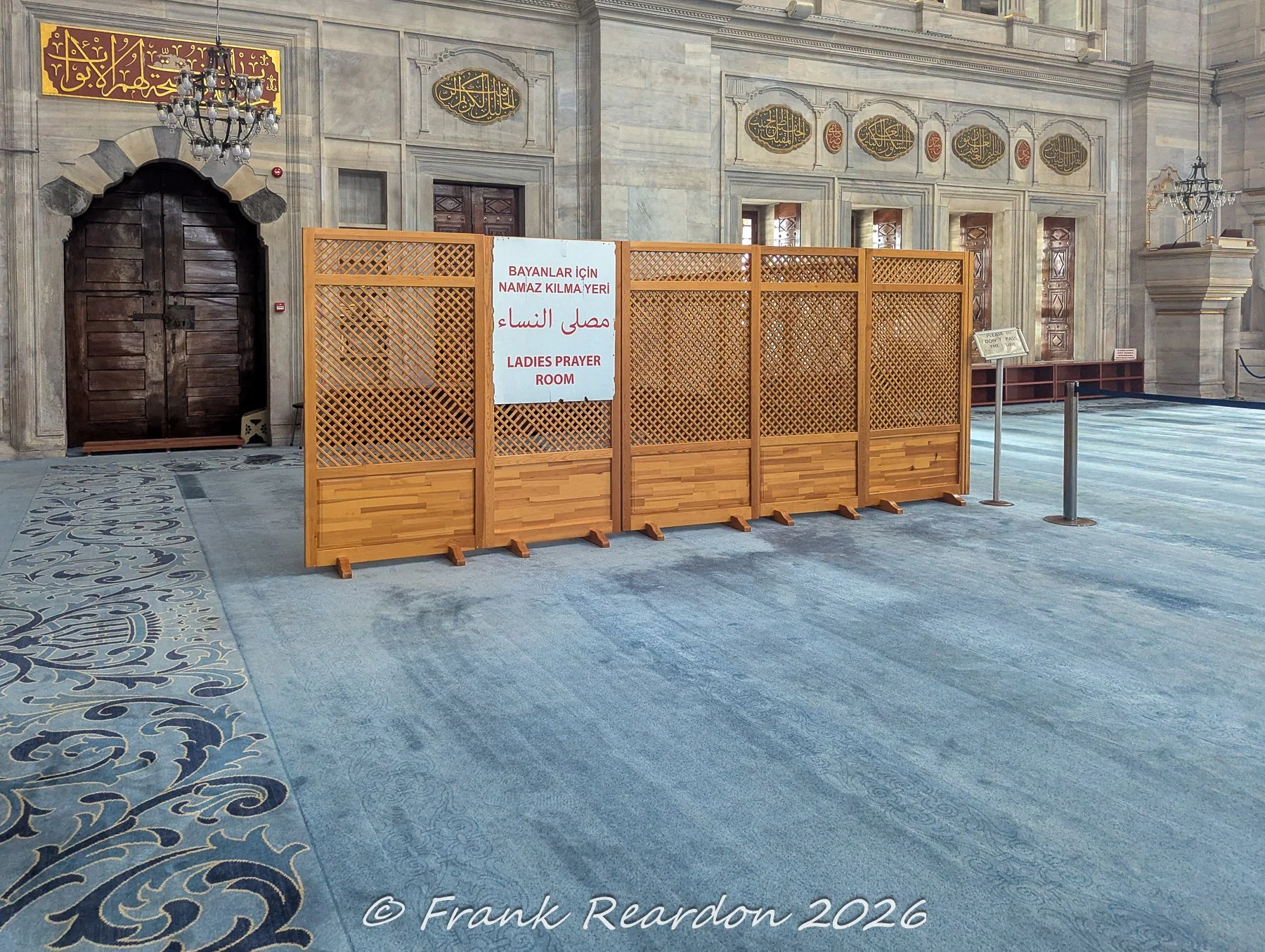 A view of the wooden lattice partition marking the designated "Ladies Prayer Room" (Bayanlar İçin Namaz Kılma Yeri) across the blue-carpeted interior of the Nuruosmaniye Mosque.