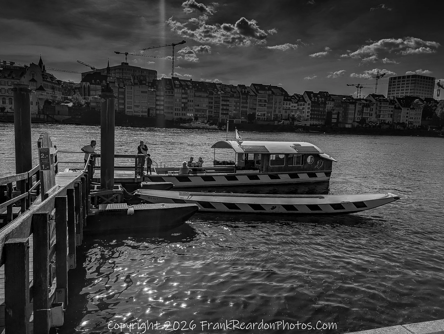 “Dockside Pause” Boats rest against the current, their reflections shimmering beneath cranes and clouds.