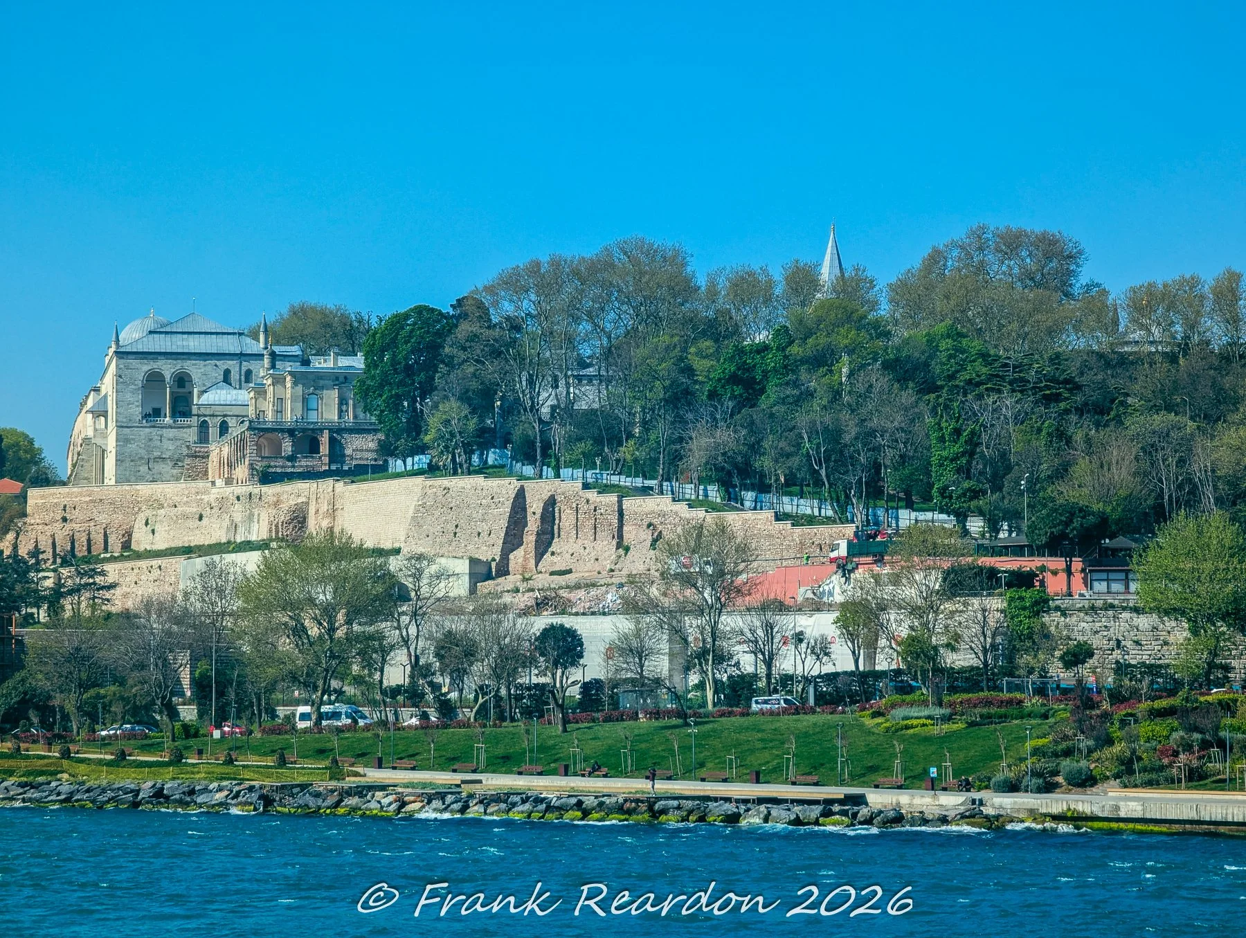 A scenic view of the ancient stone fortification walls of Topkapi Palace rising above the coastal greenery along the Bosphorus shore.