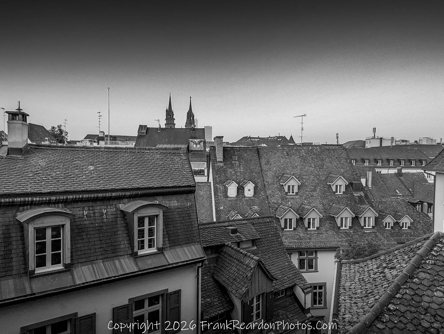 "City Rooftop View" A view overlooking various rooftops in a city with two church spires visible in the background.
