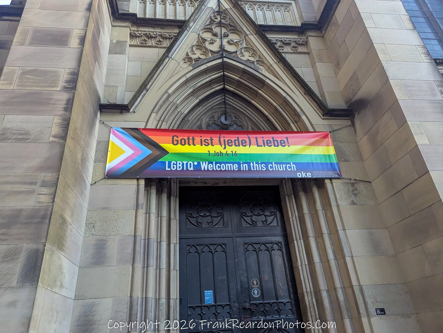 "LGBTQ+ Welcoming Church" A stone church entrance decorated with a rainbow flag banner that reads "Gott ist (jede) Liebe!" and "LGBTQ* Welcome in this church".
