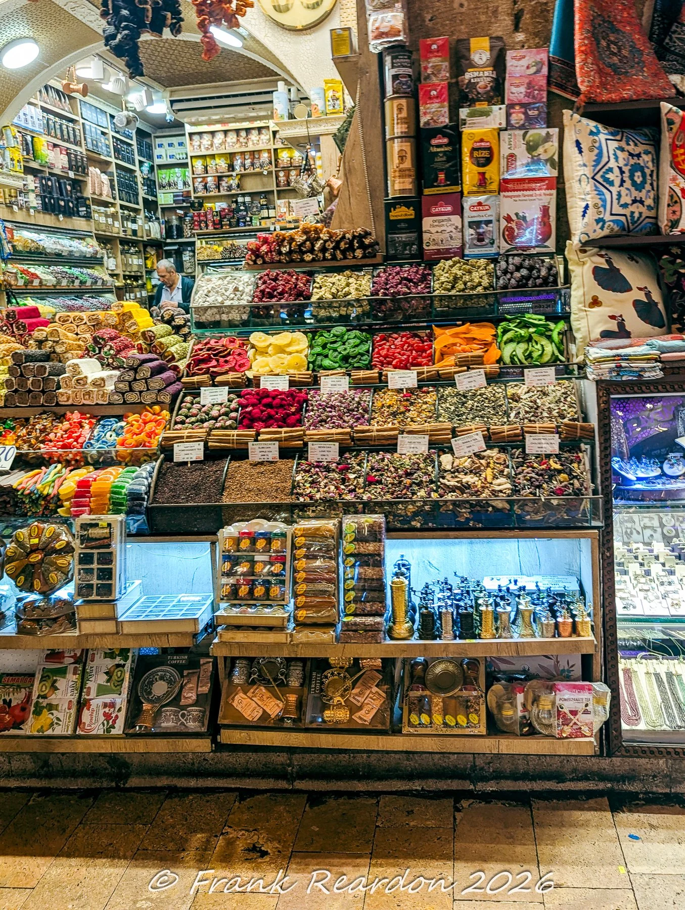 A rich, colorful stall overflowing with rows of traditional Turkish delights, dried fruits, flower petals, and spice containers inside the Spice Bazaar (Misir Carsisi).