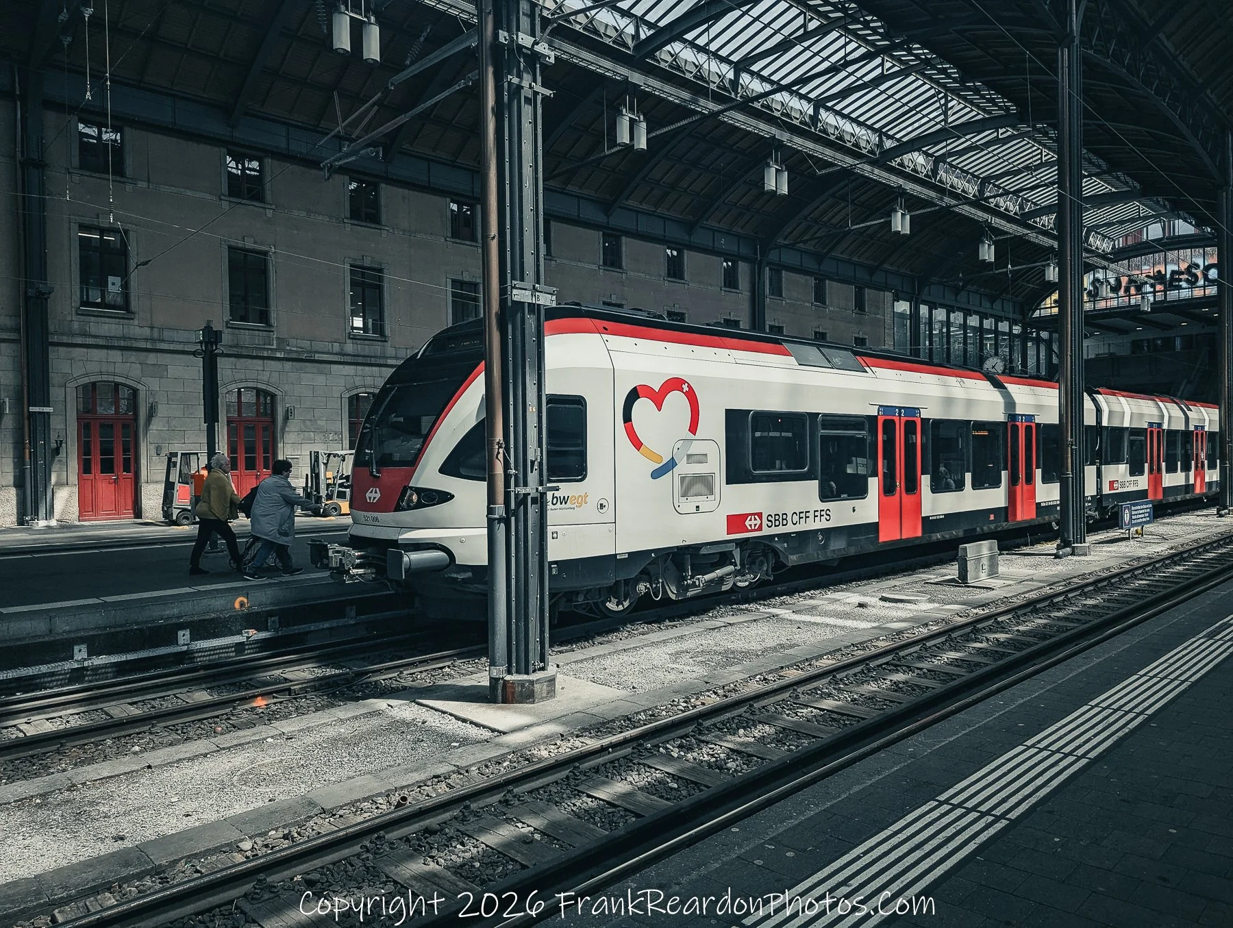 “Heart of Transit” A Swiss train waits under the glass canopy, its emblem of love echoing the human connections of travel.