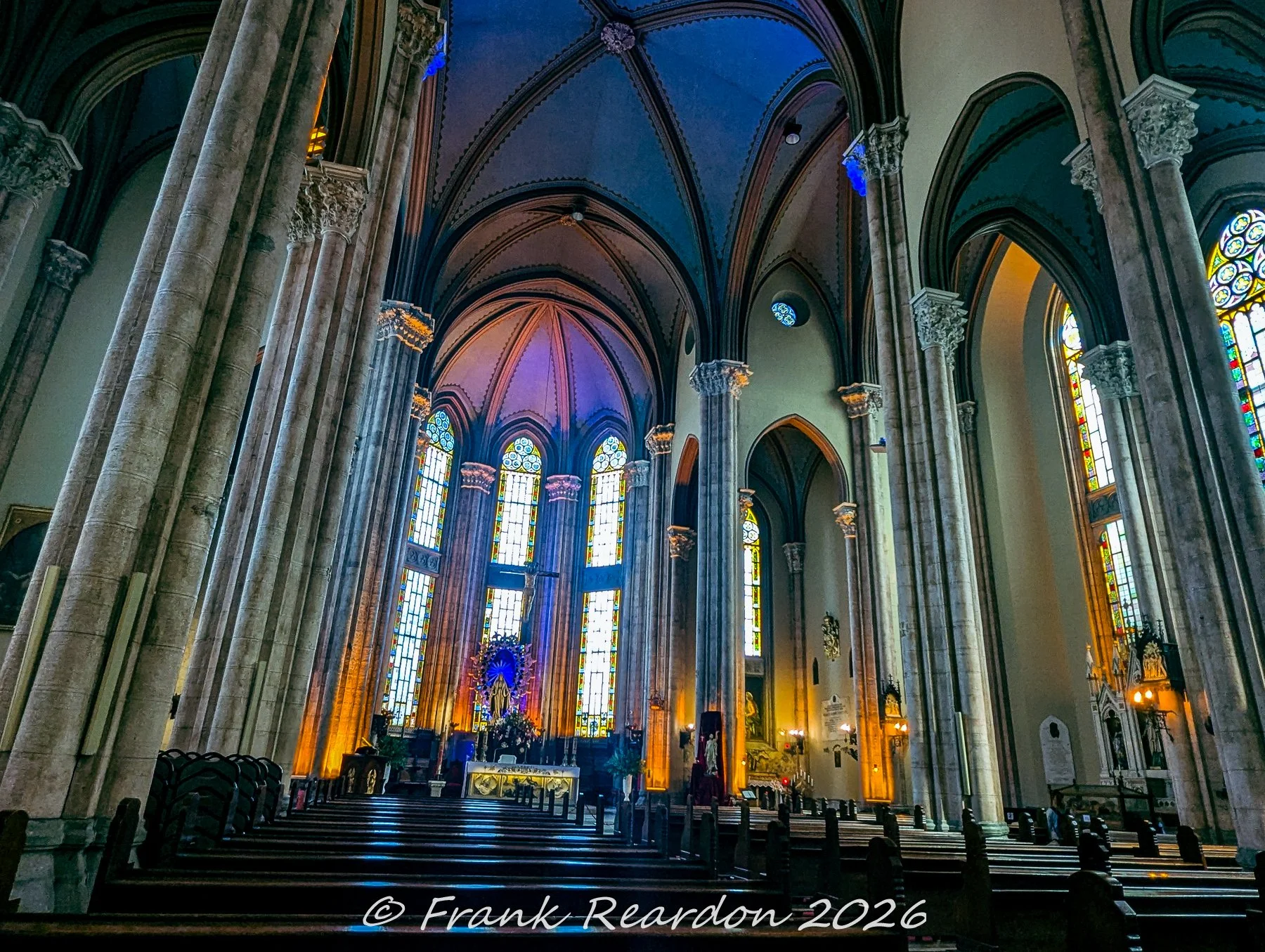 A perspective from the wooden pews looking down the central aisle toward the brightly lit altar and sanctuary of the Church of Saint Anthony of Padua.