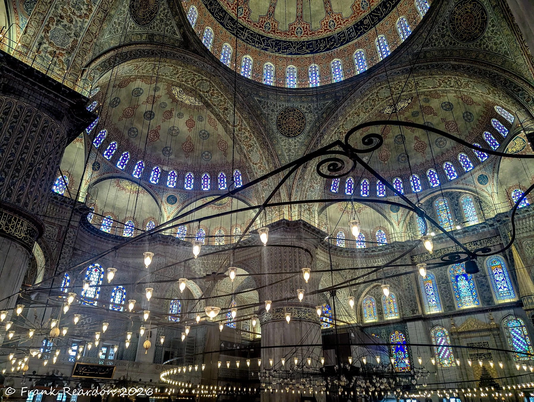 A wide-angle view of the cavernous interior, showcasing layers of decorated domes, geometric patterns, and rows of colorful stained-glass windows.