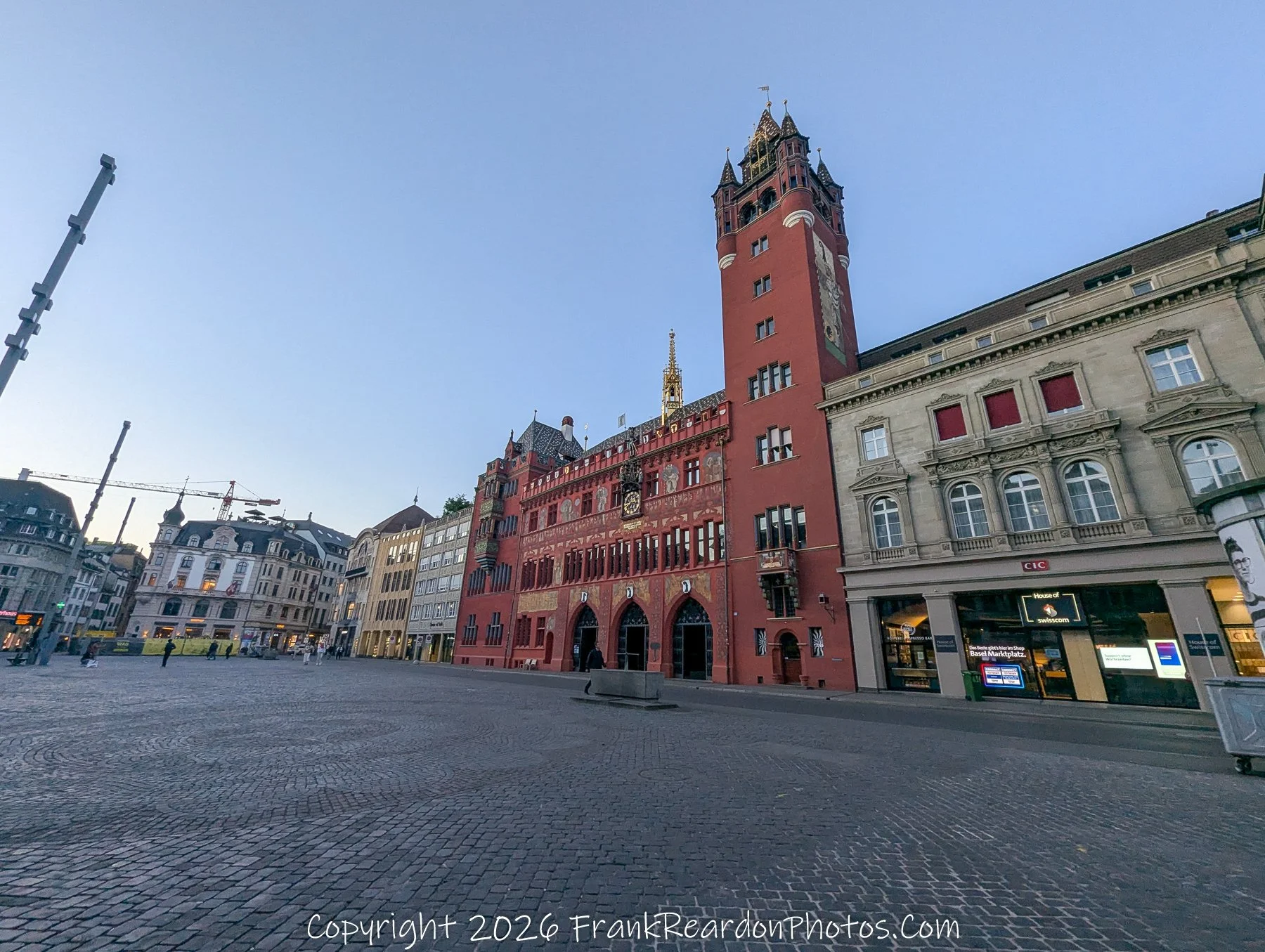 "Sunset at the Rathaus" A wide-angle shot of the iconic, red-sandstone Basel Town Hall (Rathaus) situated in the quiet, cobblestoned Marktplatz during the late afternoon.