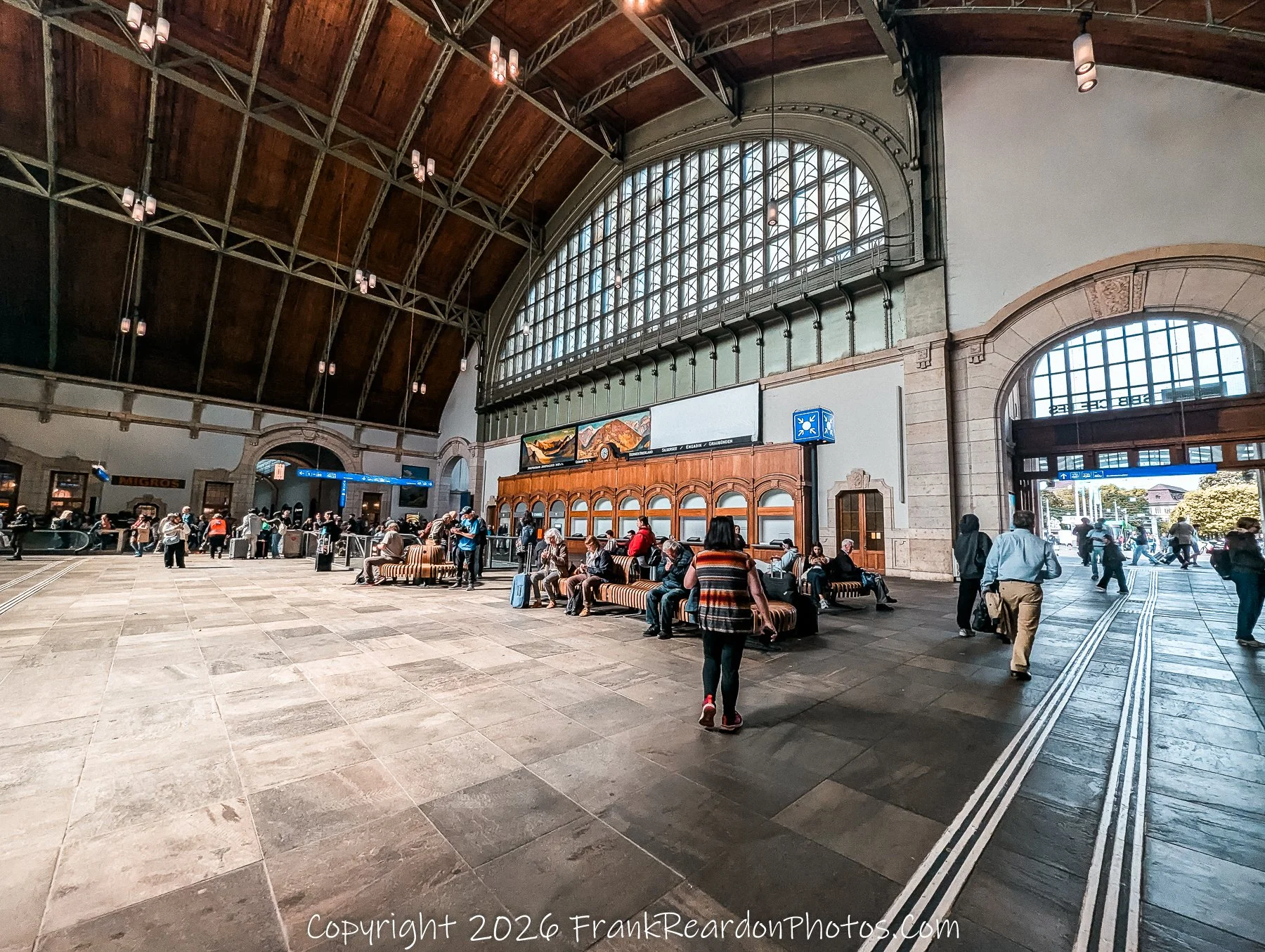 “Waiting and Wandering” Travelers rest beneath vaulted wood and glass, suspended between arrival and departure.