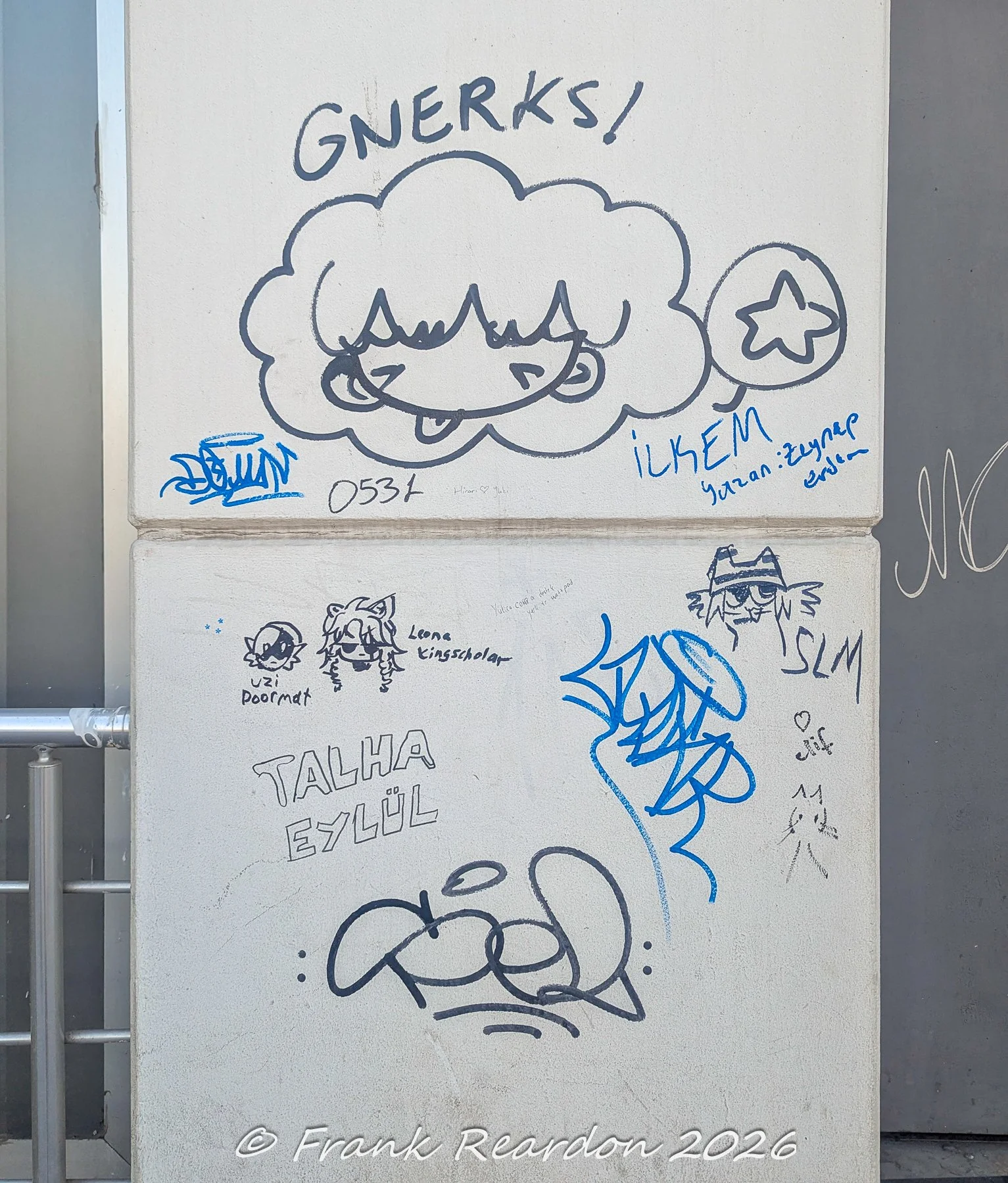 A textured concrete pillar adorned with playful blue marker drawings, cartoon cloud characters, and handwritten names.