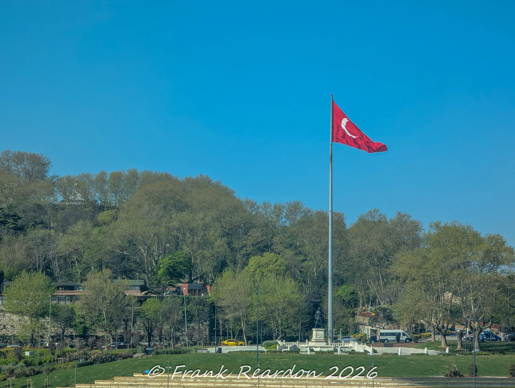 A massive Turkish flag flying proudly atop a tall flagpole overlooking the green parklands and coastal promenade at Sarayburnu.