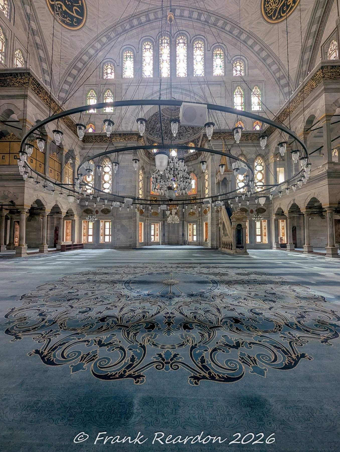 A wide-angle view across the expansive, ornate blue prayer carpet toward the rear of the main interior hall at the Nuruosmaniye Mosque.