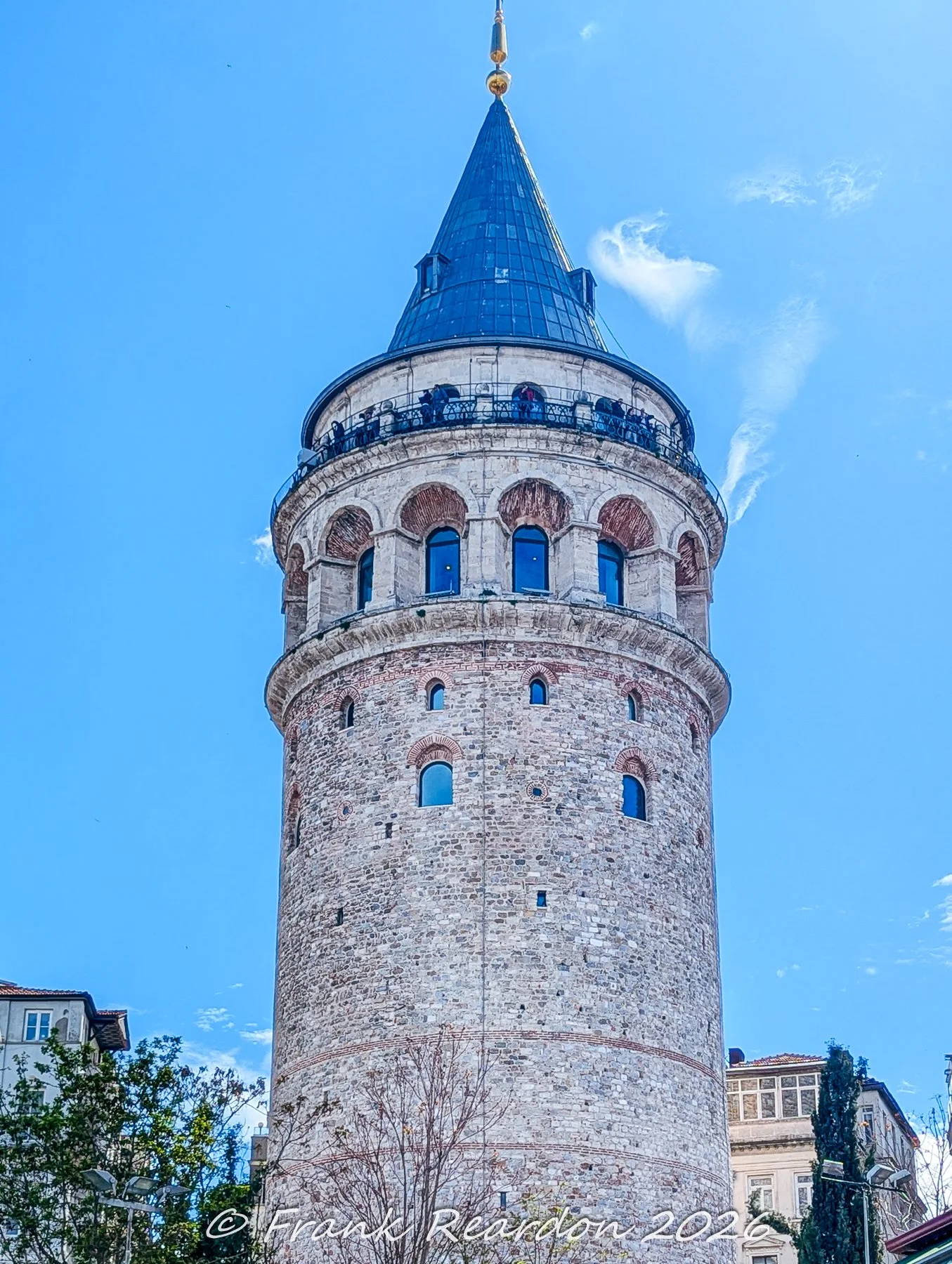 A close-up view of the upper stone facade, arched windows, and observation deck of the medieval Galata Tower.