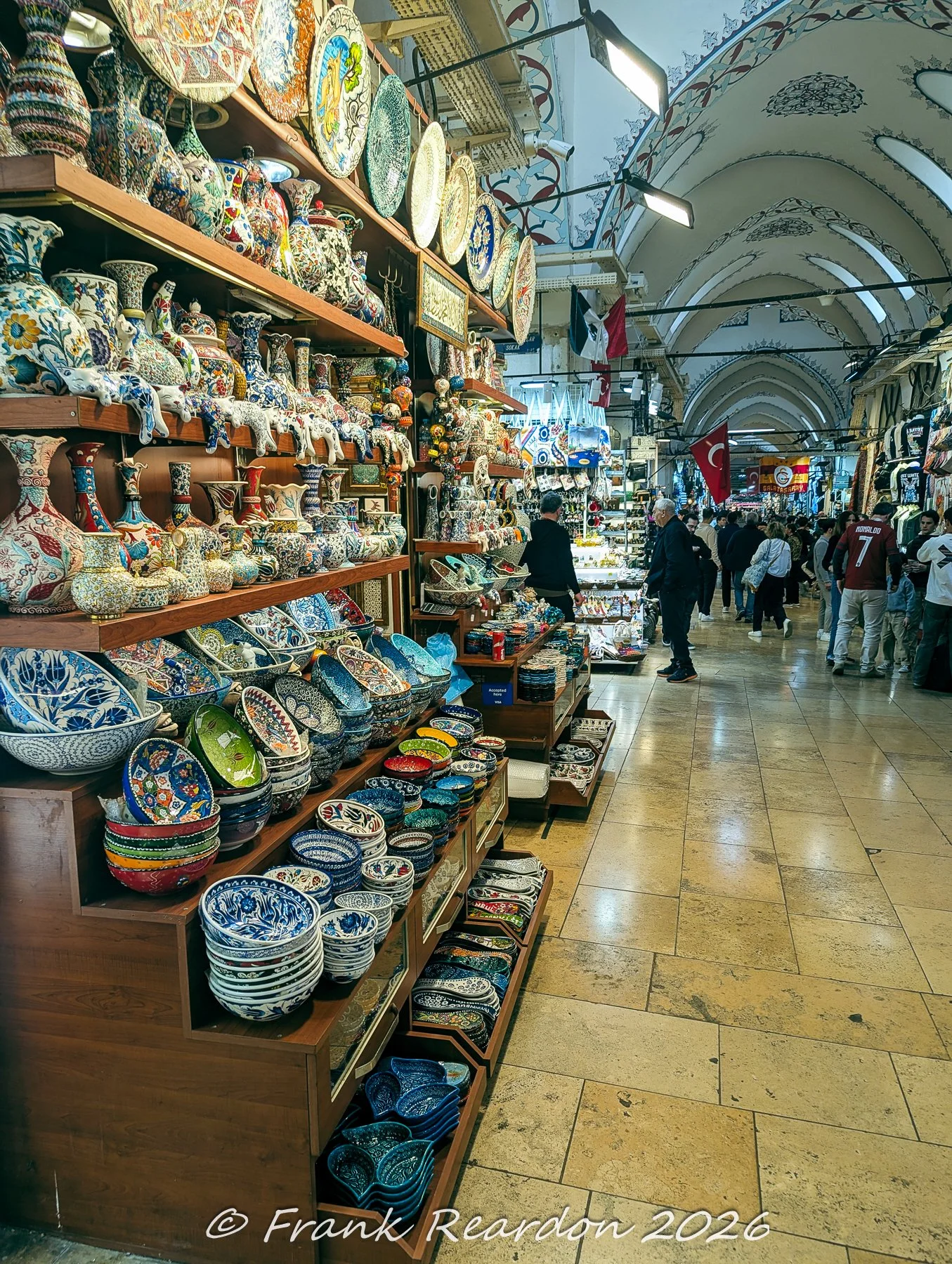 Shelves packed with vibrant, hand-painted Turkish ceramic plates, bowls, and vases lining a shop inside the historic Grand Bazaar.