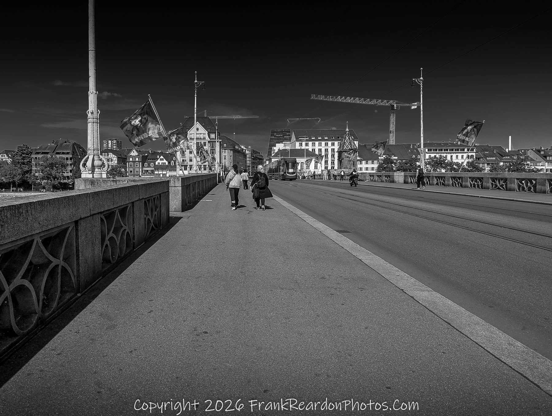 “Crossing Light” Pedestrians and trams share the bridge’s quiet symmetry under a sky of deep contrast.