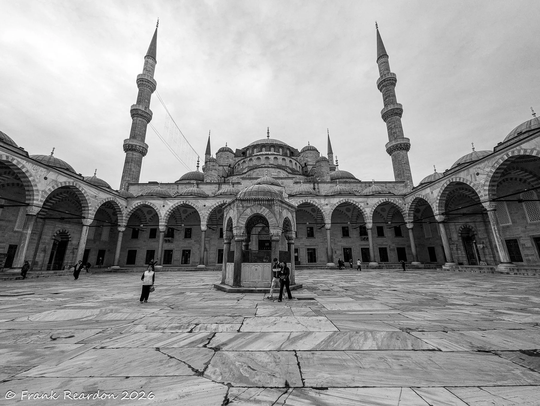 A wide black-and-white composition of the sweeping marble courtyard, framed by twin minarets and the classic domes of the structure.