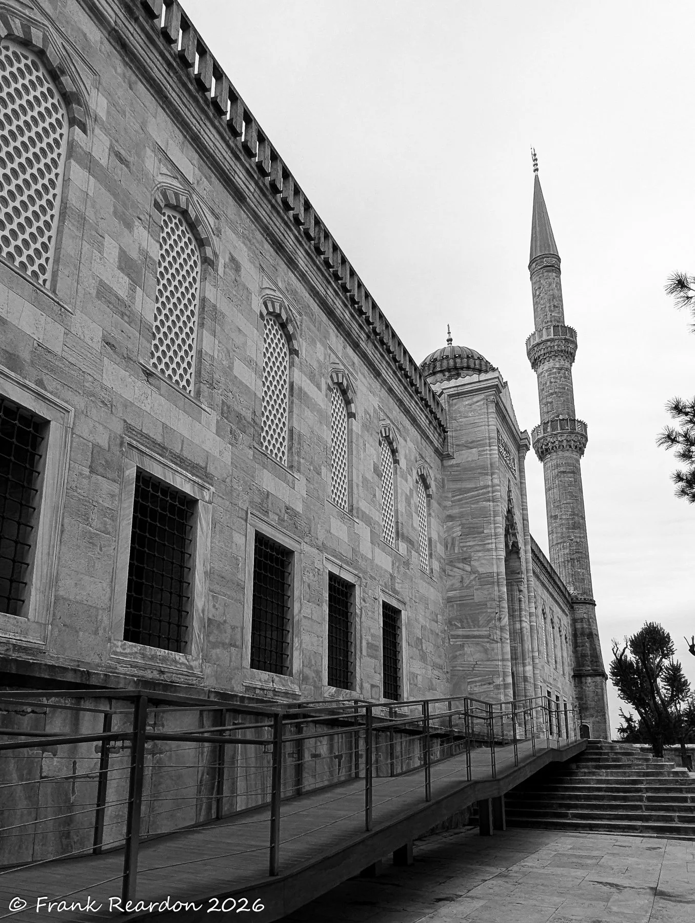 A dramatic black-and-white perspective capturing the historic stone architecture, arched windows, and towering minaret of the mosque.