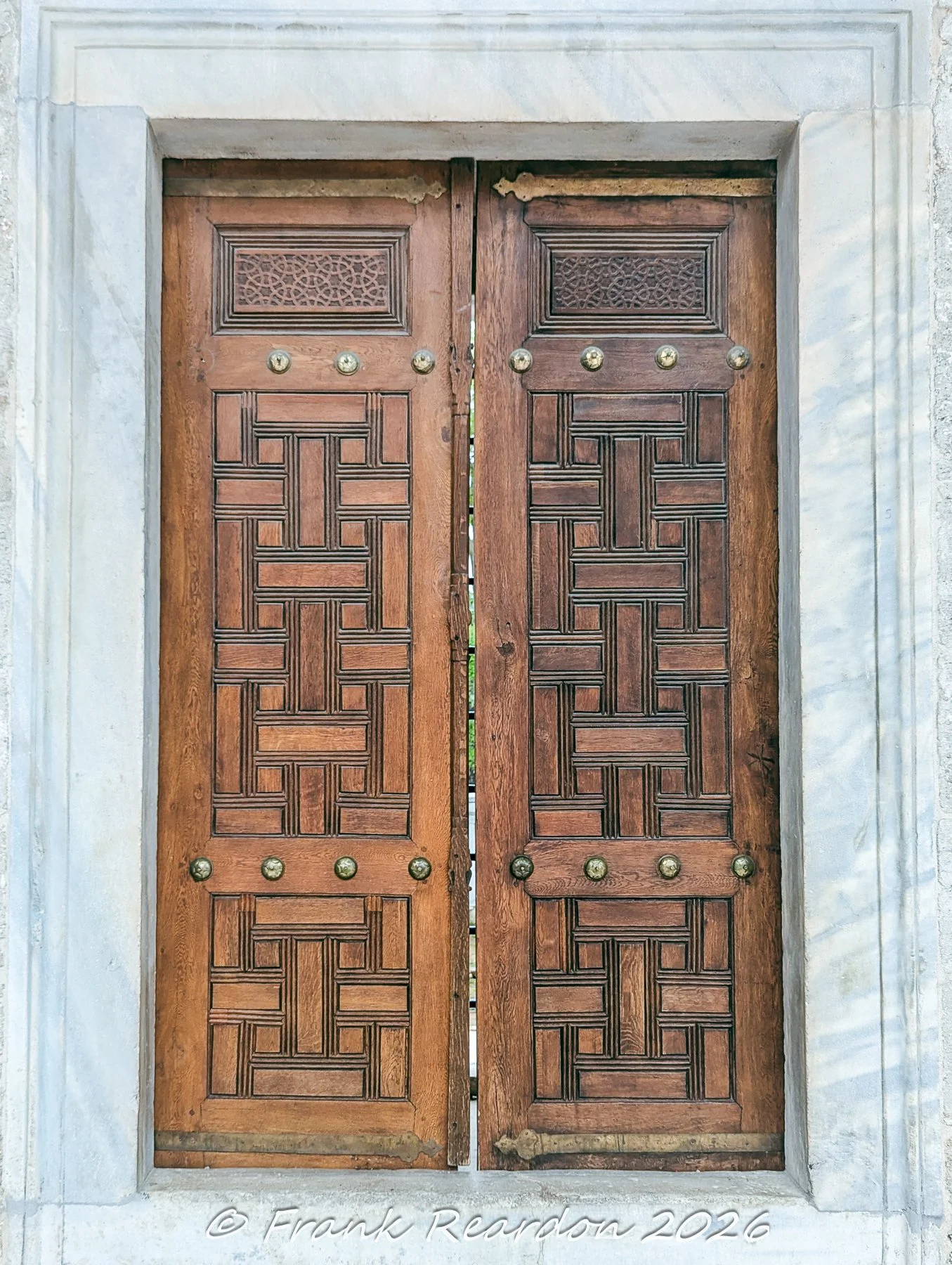 A close-up view of intricate geometric wooden carving and brass decorative fixtures on a doorway within the Blue Mosque complex.