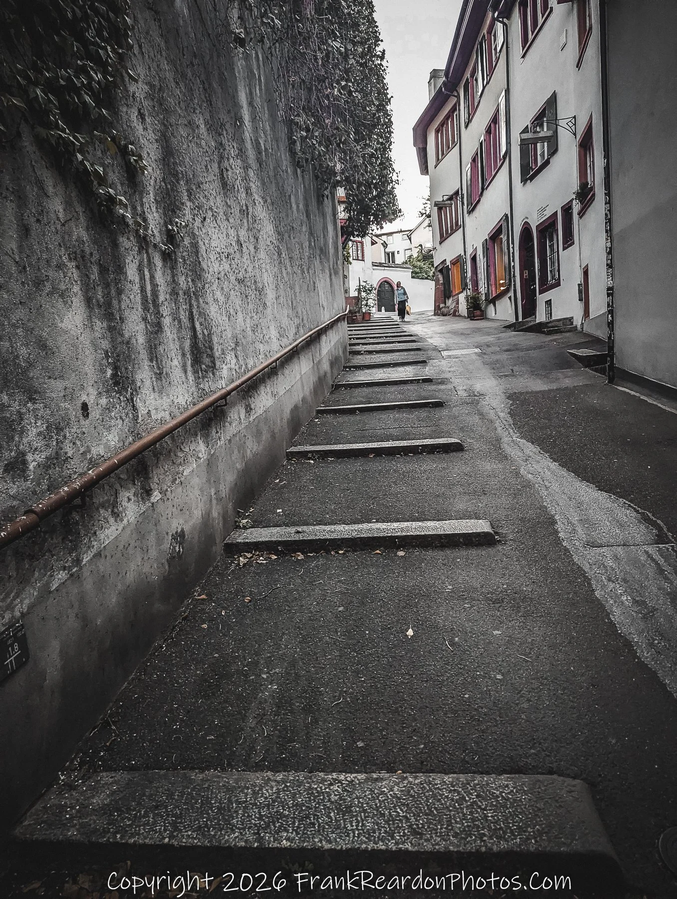 "Stone Staircase Path" An outdoor stone staircase leading up between two buildings with a pedestrian walking in the distance.