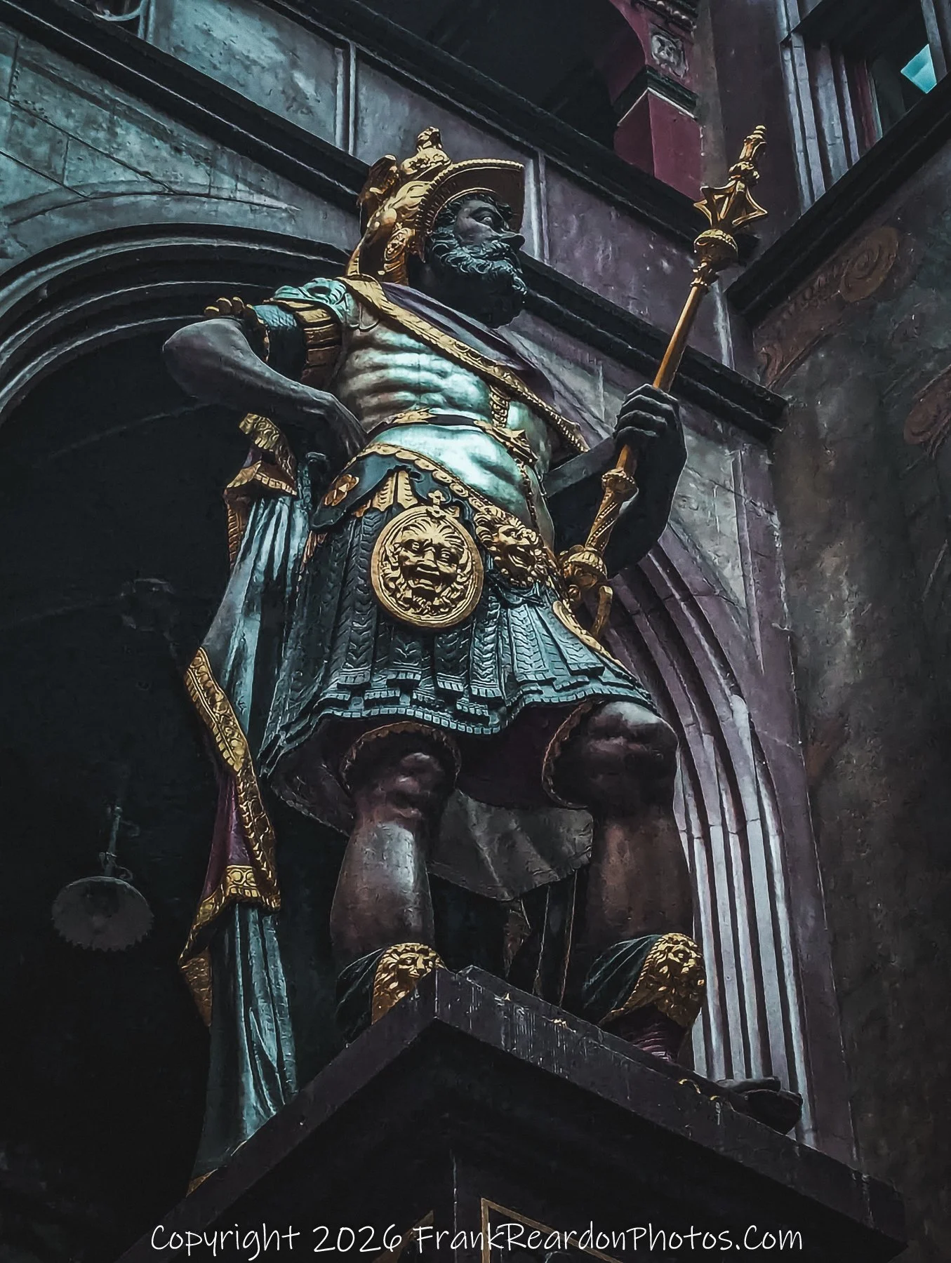 "The Golden Sentinel" A close-up, upward-facing view of a detailed, regal statue holding a staff, standing prominently within a stone-arched environment.