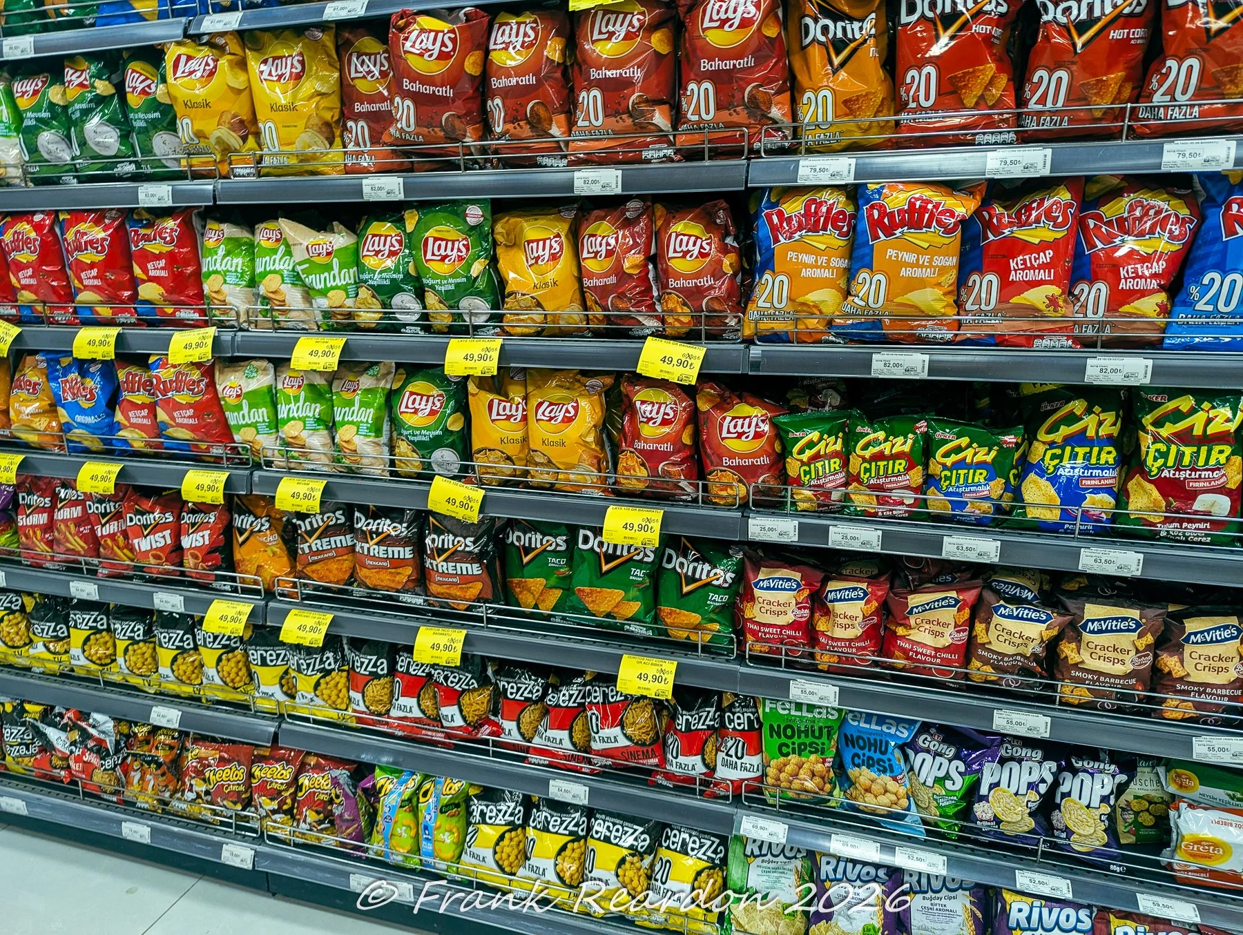 A supermarket aisle neatly stocked with various brands of chips, crackers, and savory snacks.