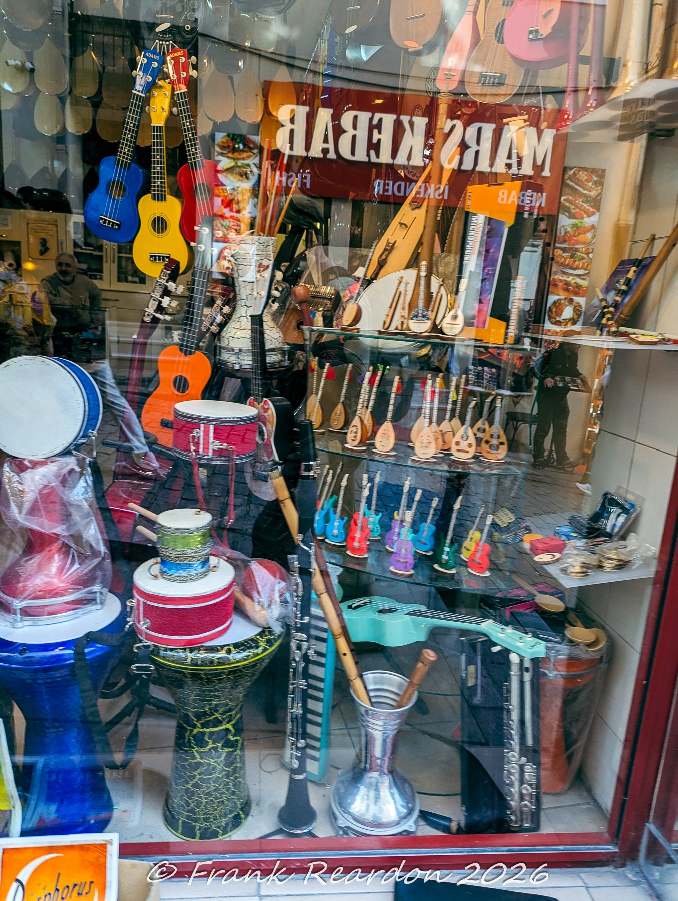 A storefront window showcasing a diverse collection of musical instruments, including ukuleles, traditional drums, stringed instruments, and flutes.