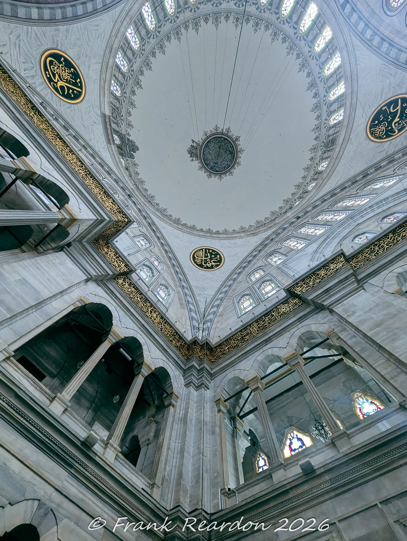 A close perspective of the grand white marble ceiling, central medallion, and golden calligraphic roundels inside the main hall of the Nuruosmaniye Mosque.