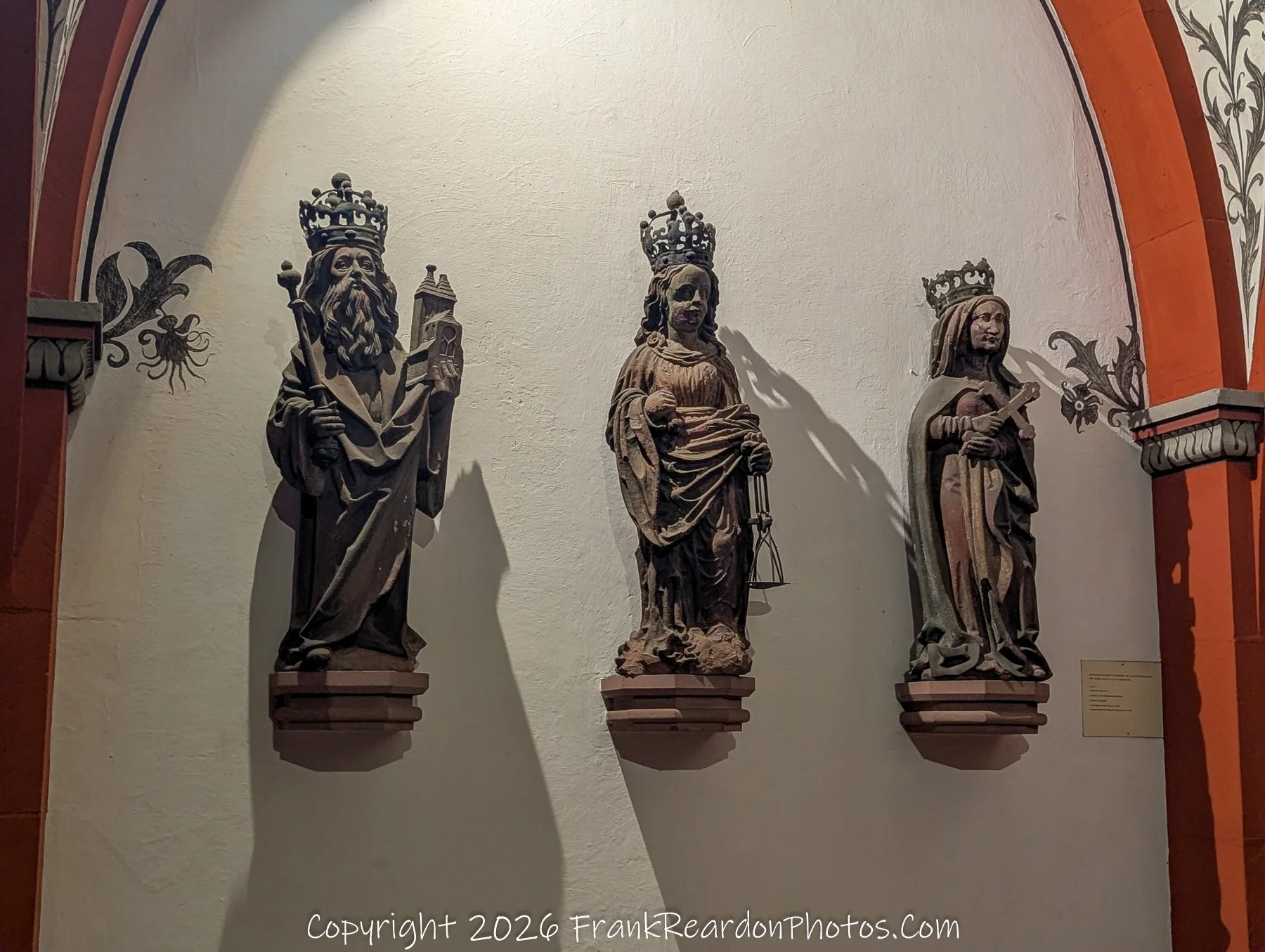 "Historic Statuary" A display of three weathered, crown-wearing stone figures mounted against an arched wall, showcasing Basel's rich historical artistry.
