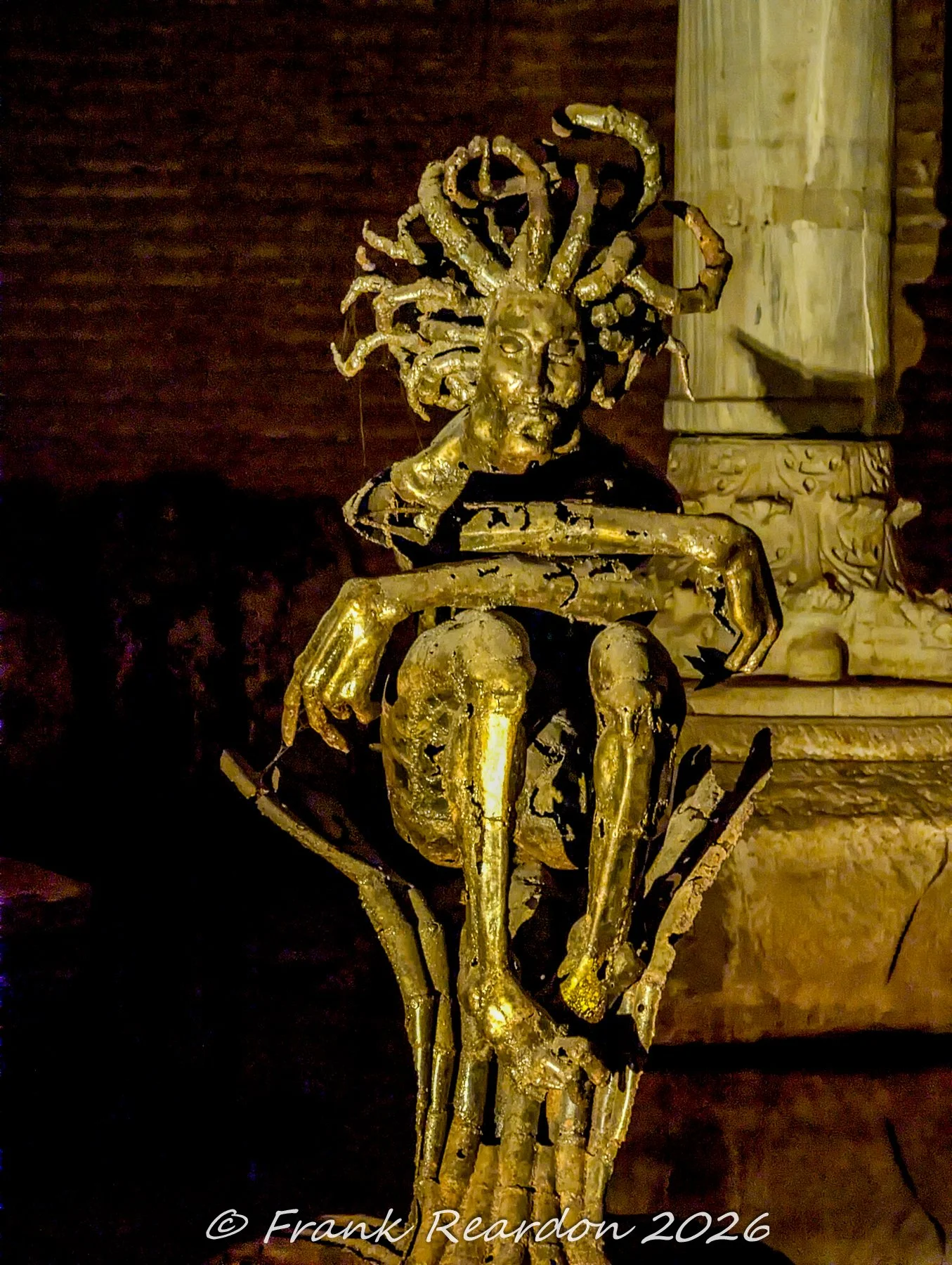 A golden, stylized statue of Medusa with snake-like hair, displayed as part of an art installation within the atmospheric chamber of the Basilica Cistern.