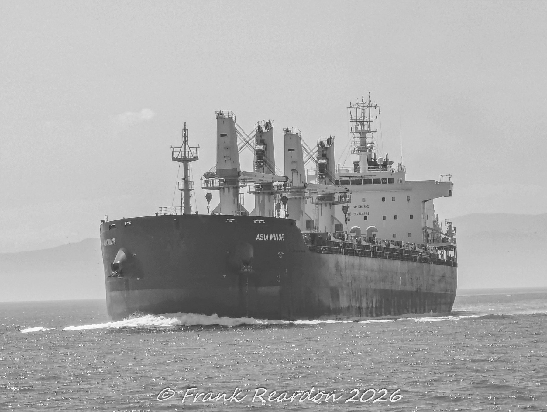 A monochrome maritime shot of the bulk carrier Asia Minor equipped with heavy deck cranes, steaming across the open sea.