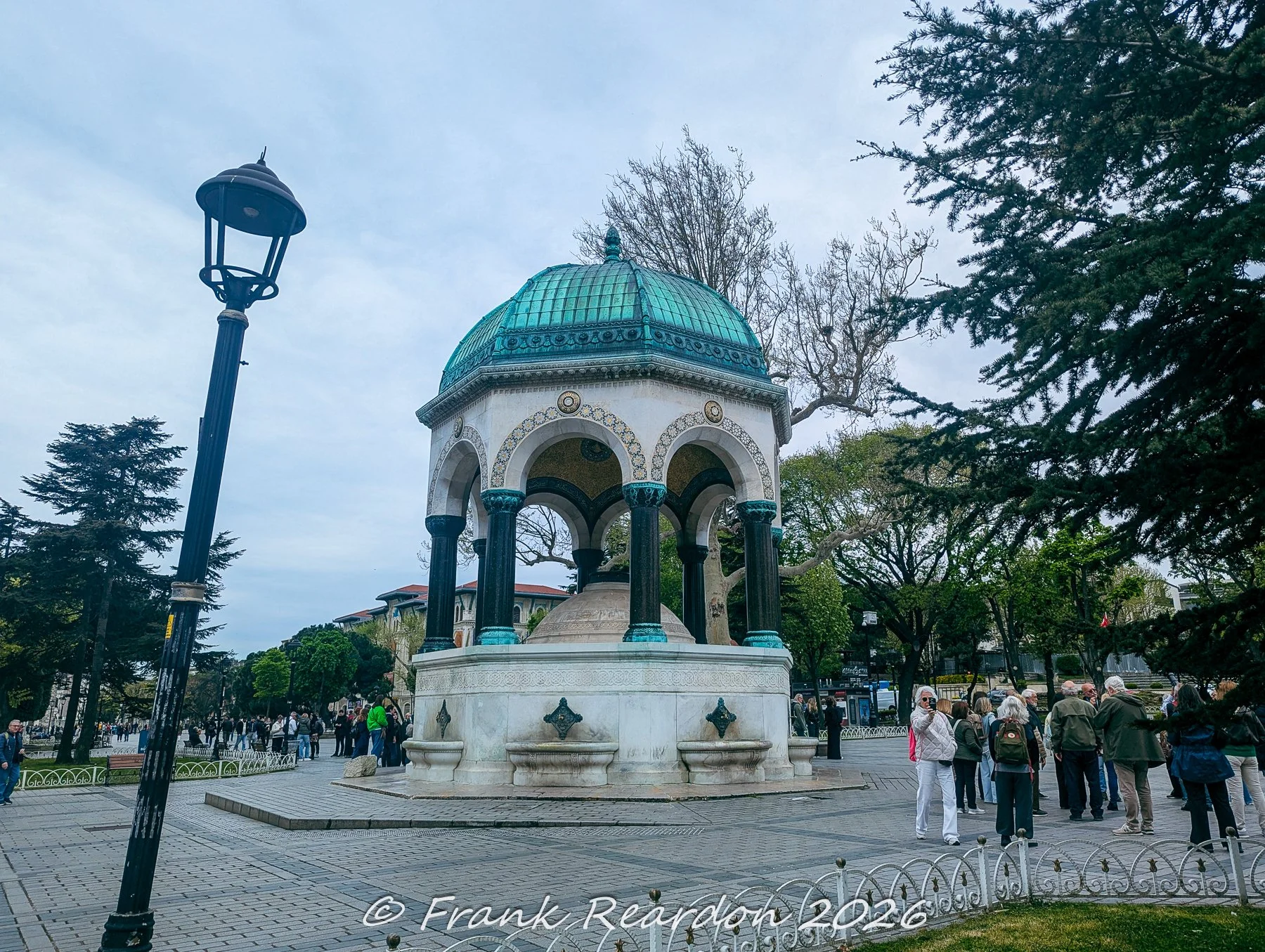 An eye-level shot of the ornate neo-Byzantine German Fountain featuring a copper-domed roof and marble columns, situated in the historic Hippodrome area.