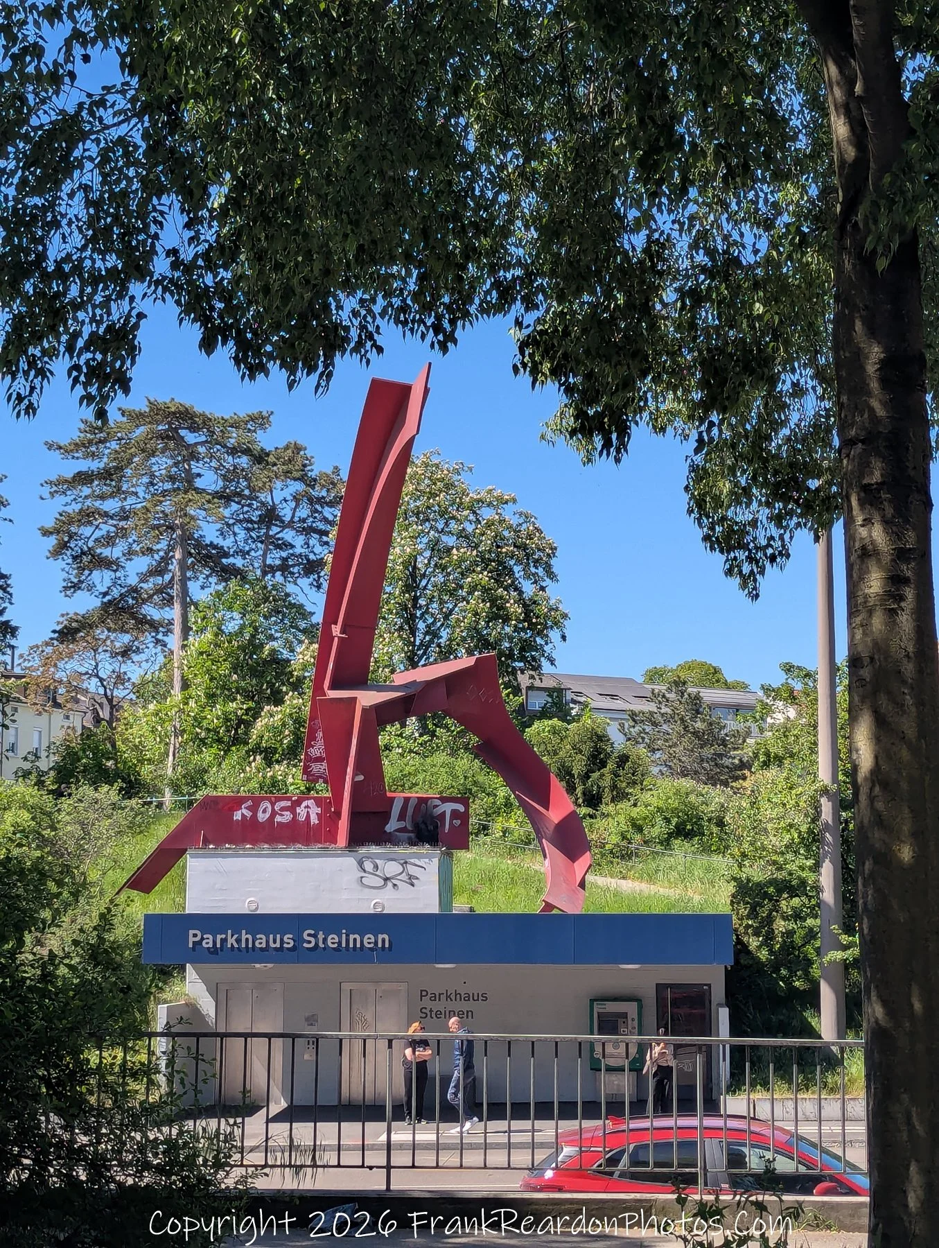 "Modern Landmark" A bright, daytime view of the entrance to Parkhaus Steinen, featuring a striking, oversized abstract red sculpture on the roof.