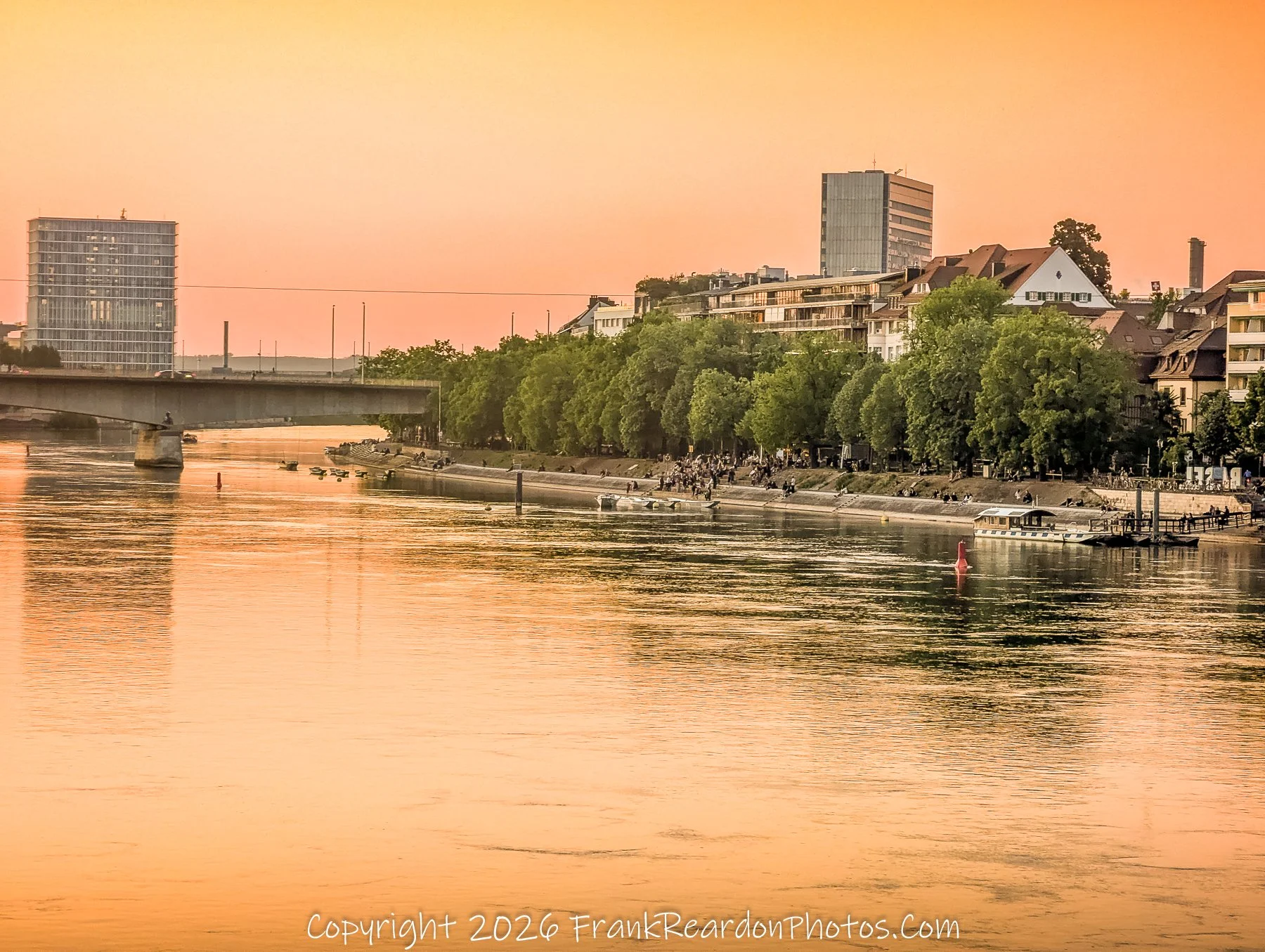 "Riverside Twilight"
A view looking down the river at sunset, capturing the calm water, lush tree-lined banks, and modern architecture under a warm, golden sky.