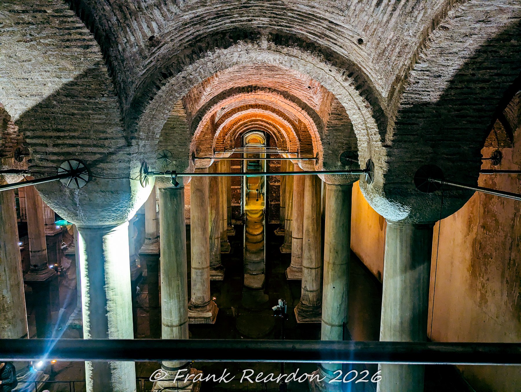 An elevated vantage point showing the historic brick arches and rows of marble columns stretching through the candlelit waters of the ancient Basilica Cistern.