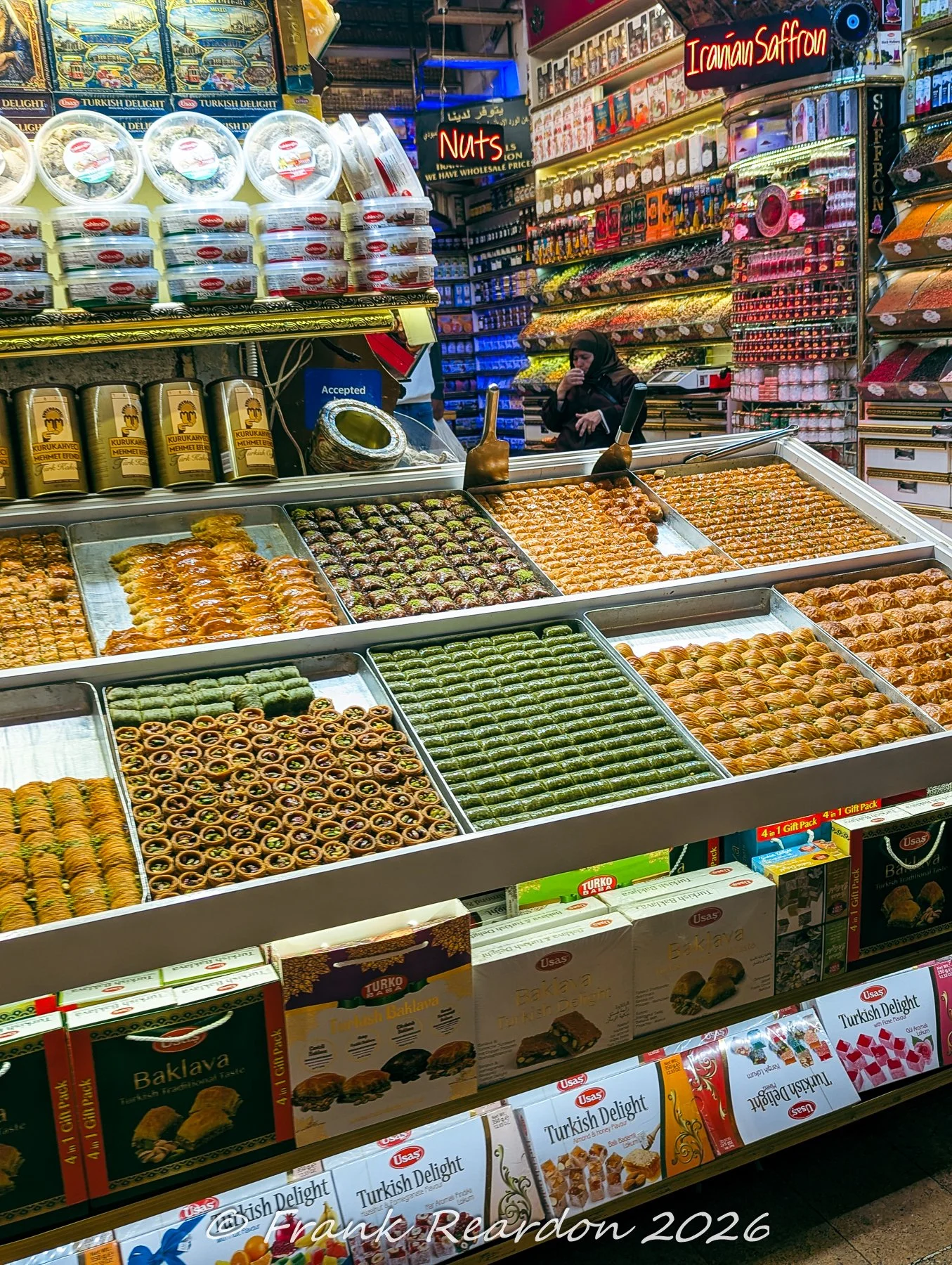 A display case filled with trays of freshly baked baklava, pistachio pastries, and packaged gift boxes inside the Spice Bazaar.