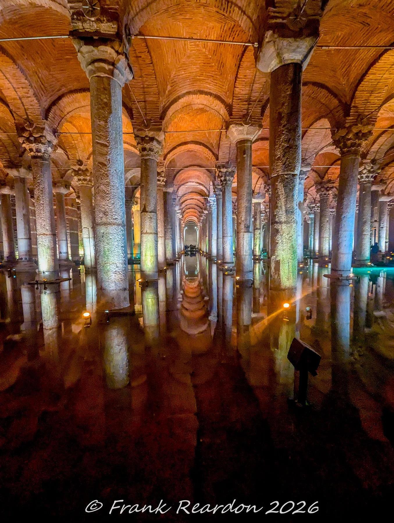 A wide-angle interior view showing the warm orange and cool blue lighting illuminating the seemingly endless rows of marble columns and vaulted ceilings reflected in the water inside the Basilica Cistern.
