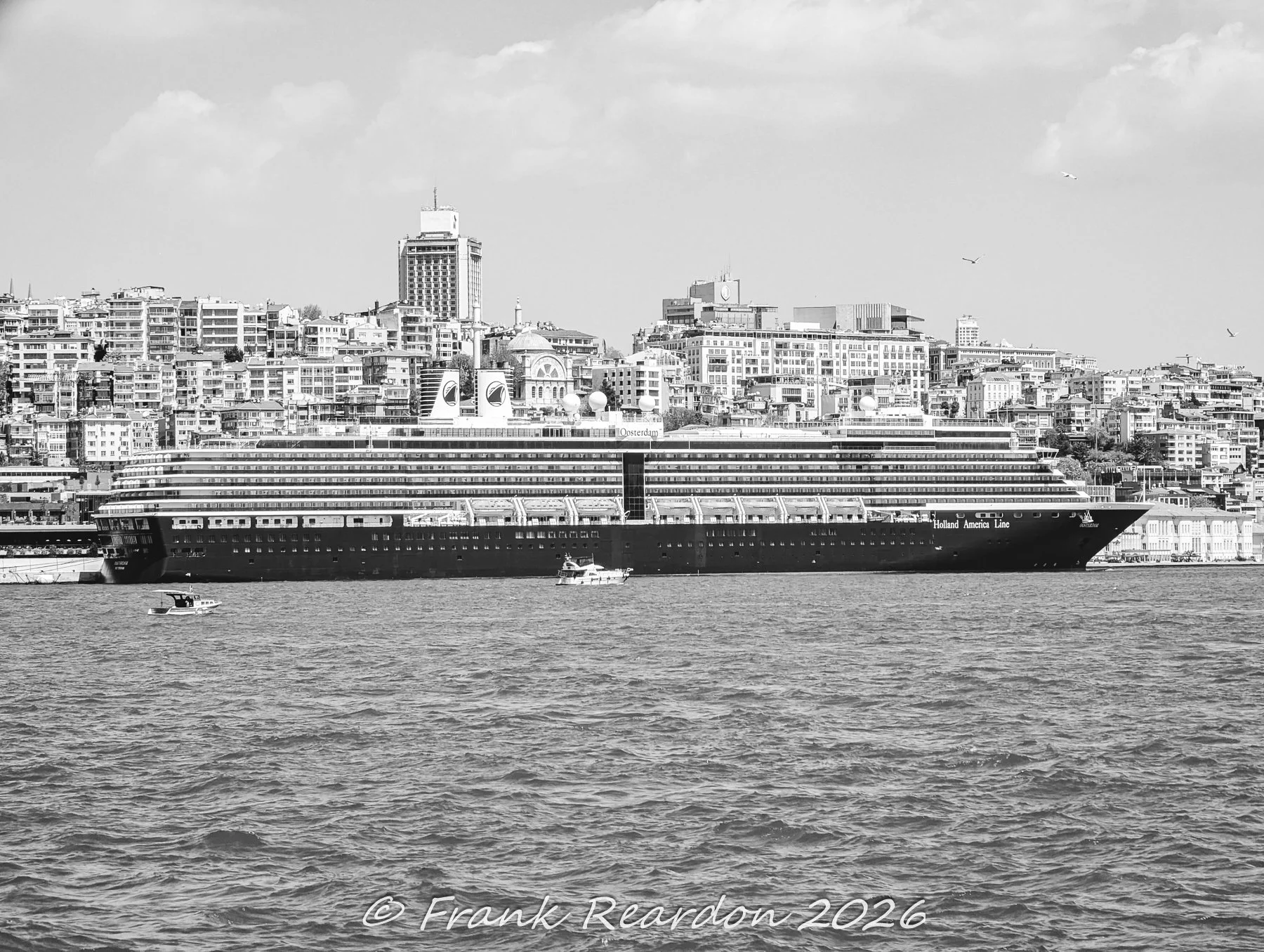 A monochrome view of a large cruise ship moored at the Karaköy coastline, with the densely built hillside architecture and a prominent high-rise hotel tower rising in the background.