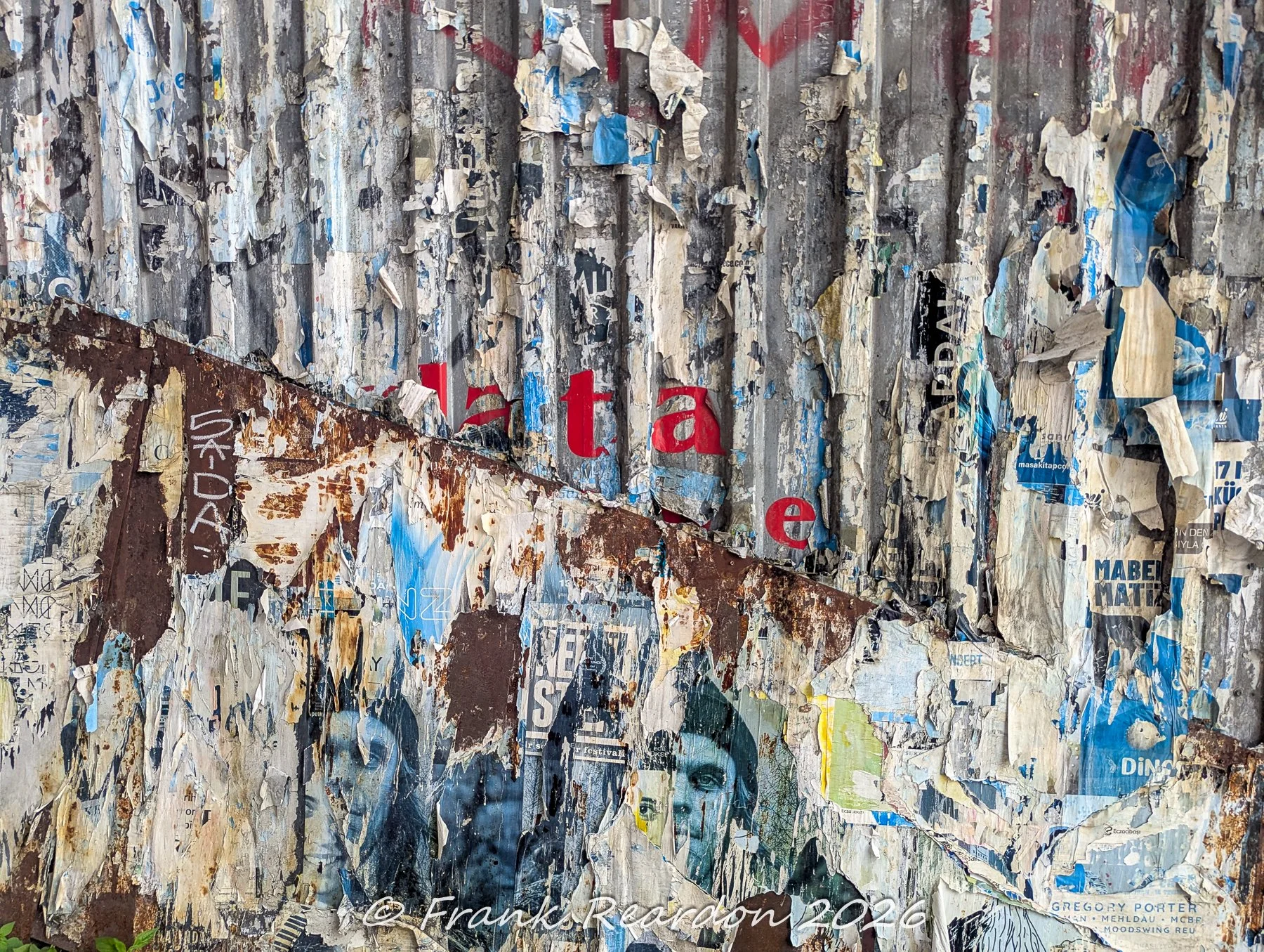 A detailed look at a weathered corrugated metal and rust wall covered with fragmented and peeling promotional flyers and posters.