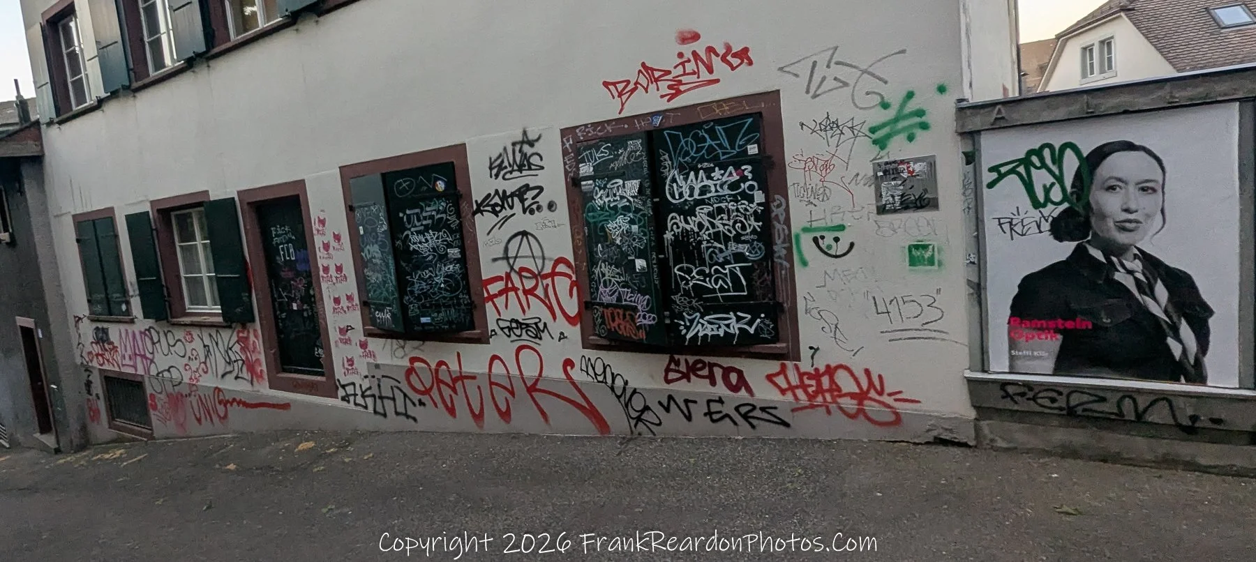 "Graffiti Wall with Poster" A building wall heavily decorated with layers of colorful graffiti and a poster of a woman.