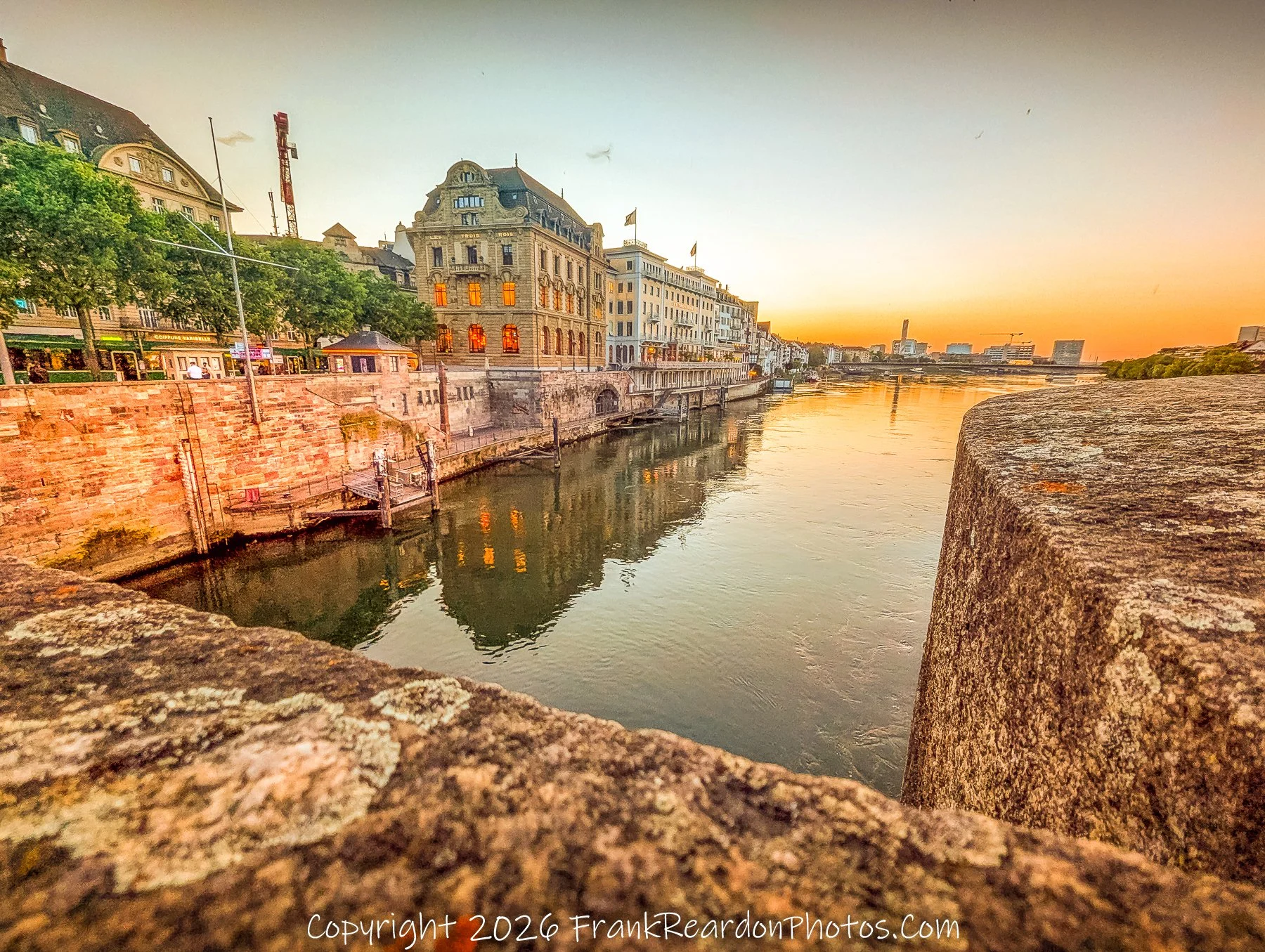 "Reflections on the Rhine" A composition looking from the edge of a stone bridge over the river, framing the historic waterfront buildings as their warm light reflects off the water's surface.