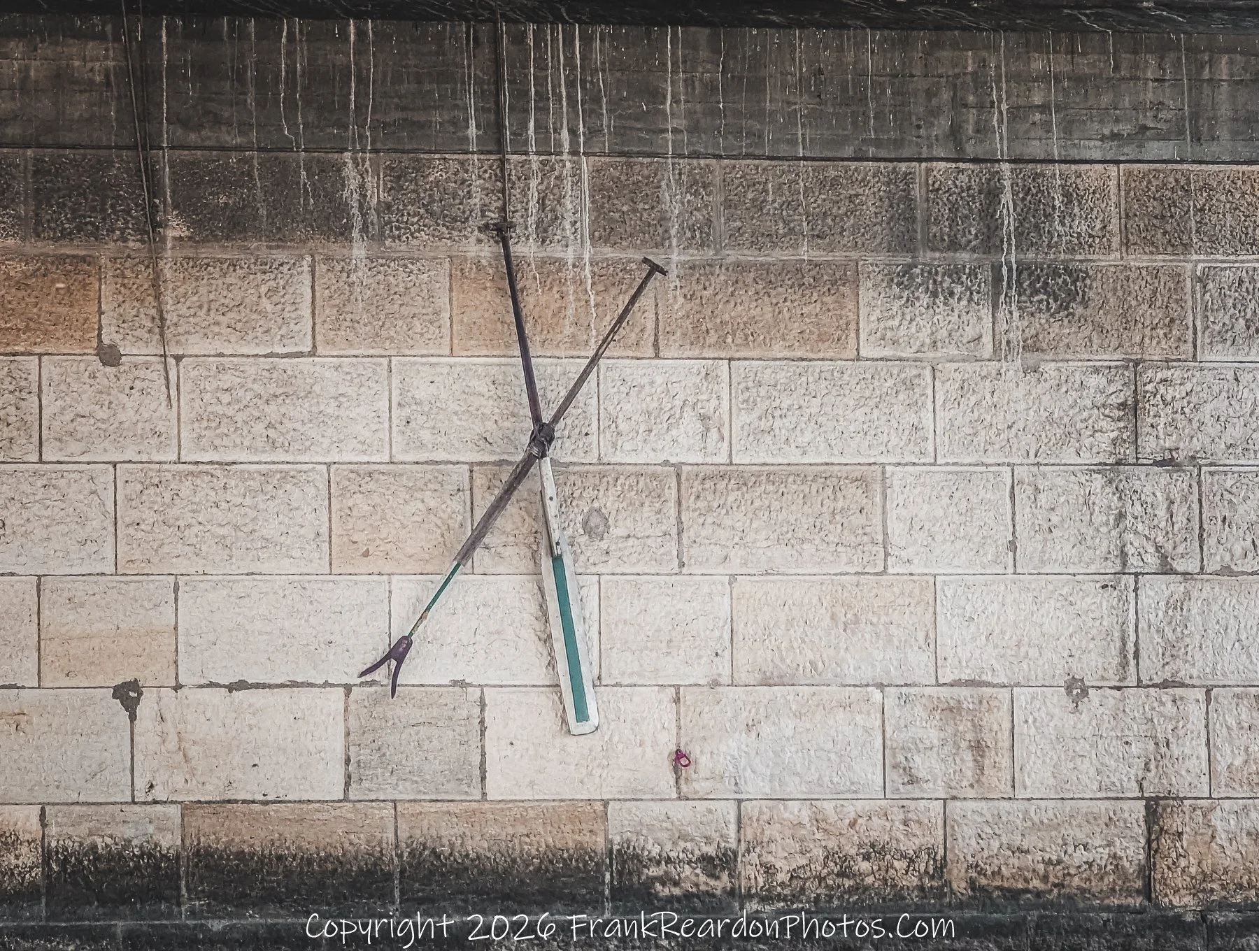 "Abstract Geometry on a Stone Wall"
A close-up of a rustic, light-colored stone wall featuring a crossing metal structure and a vertical green accent piece.