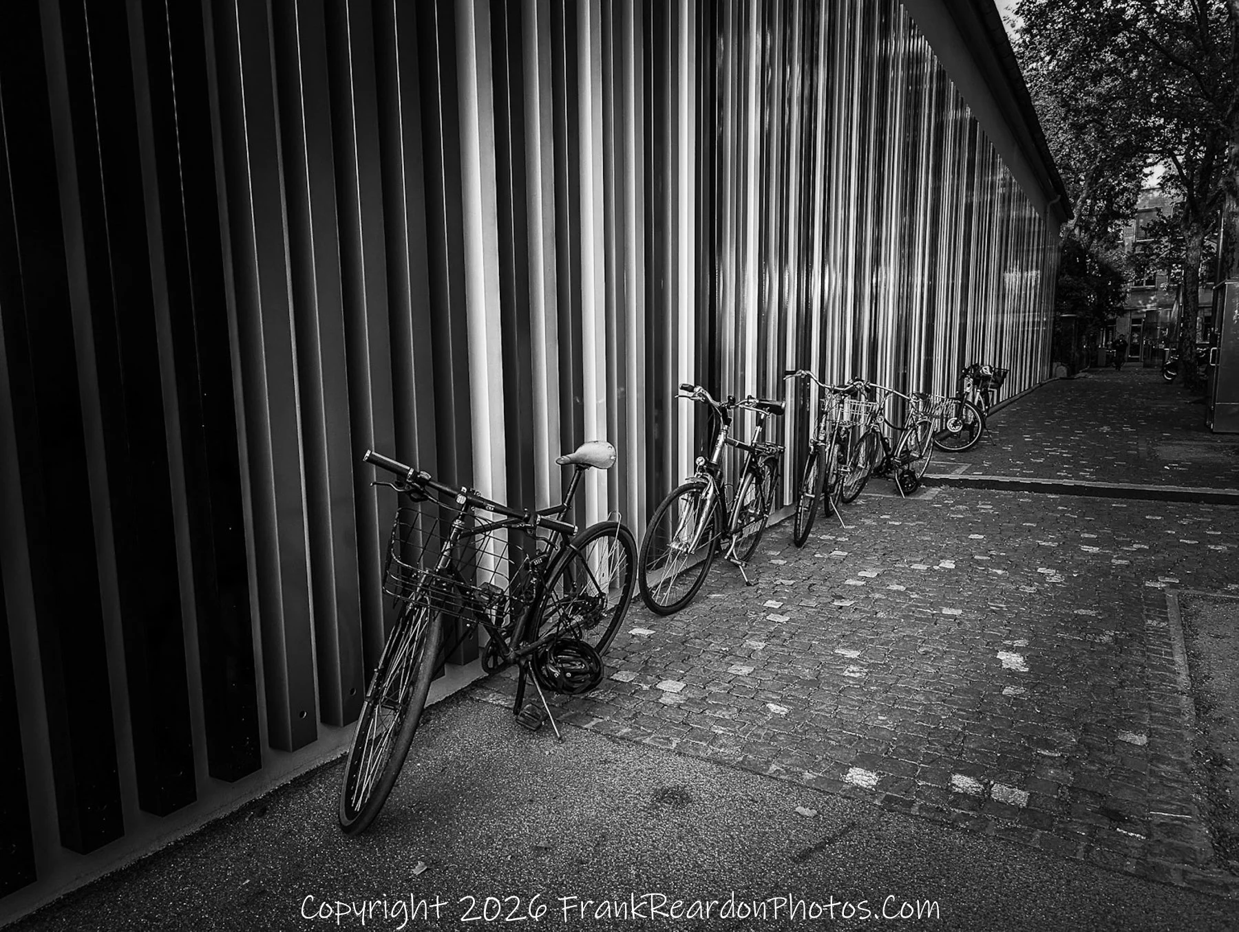 “Linear Harmony” Bicycles align against a wall of vertical reflections, merging motion and stillness in urban symmetry.