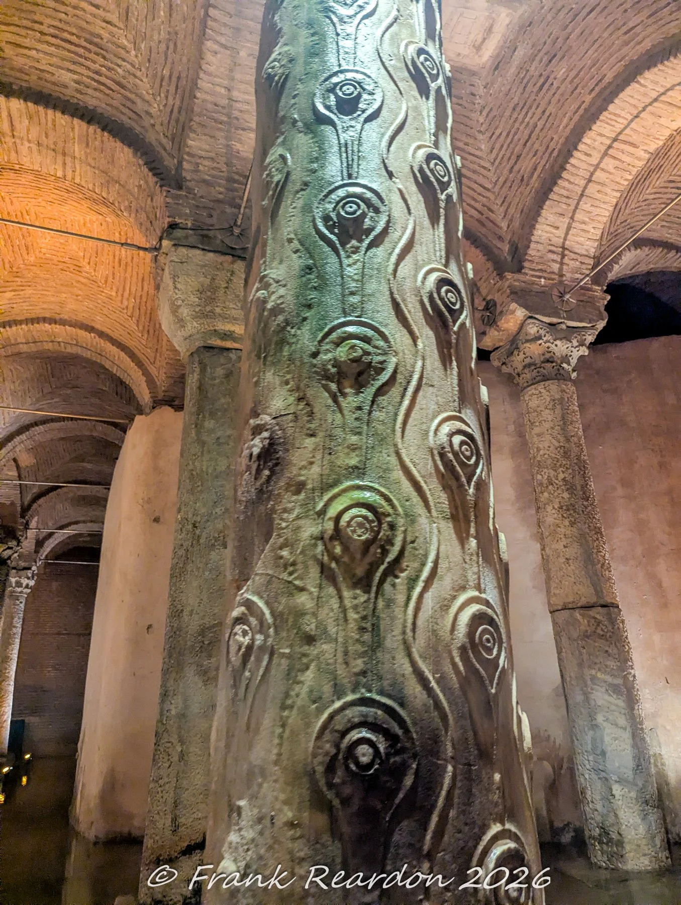 A close-up view of the famous weeping column, carved with tear-drop and "hen's eye" (Gözyaşı sütunu) patterns, surrounded by ancient brick vaulting inside the Basilica Cistern.