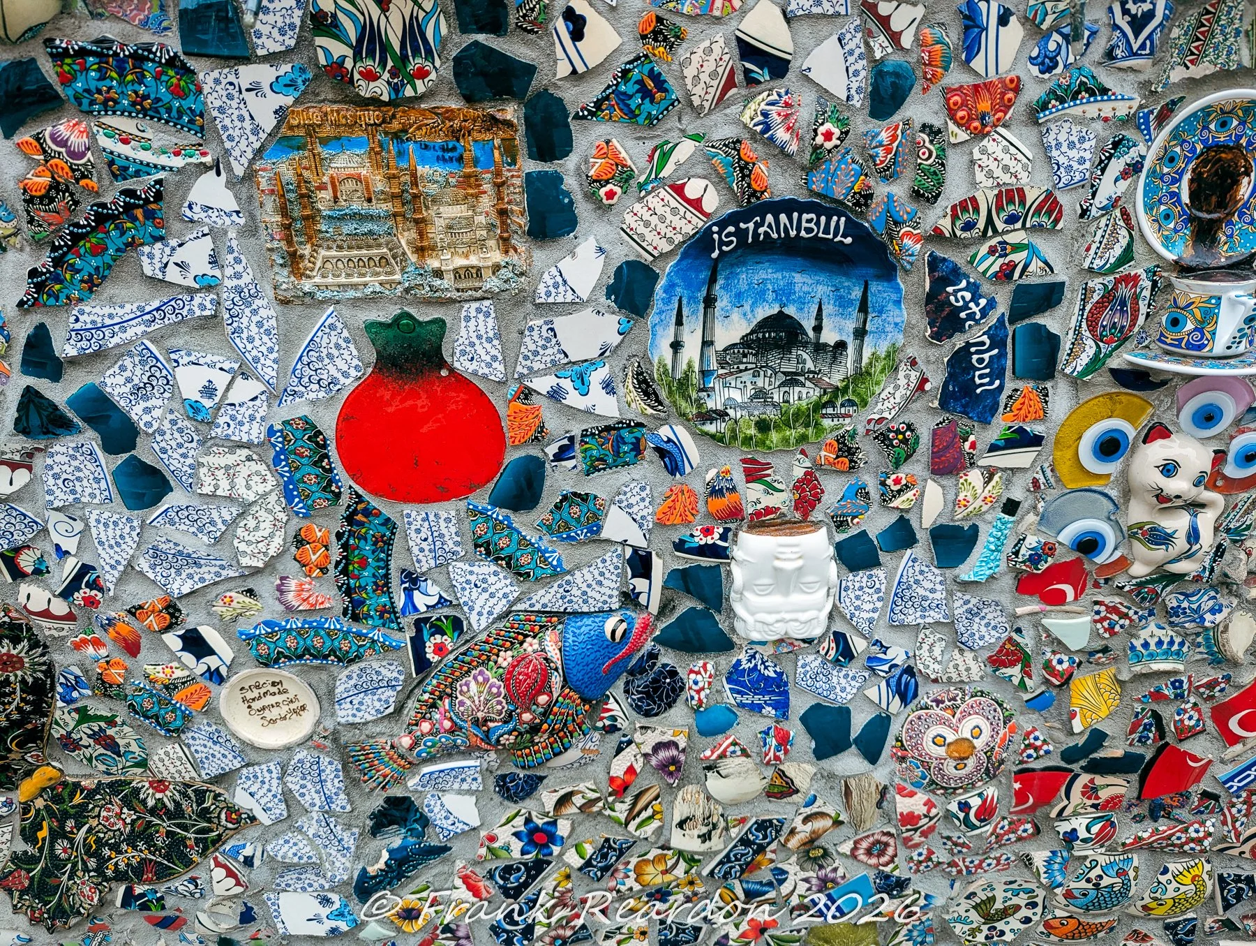 A section of an intricate street mosaic panel showcasing miniature ceramic models of Istanbul landmarks, decorative fish tiles, and traditional pottery pieces.