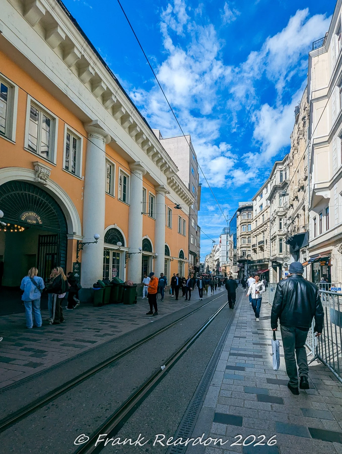 A view down Istiklal Avenue featuring classical European-style architecture, grand columned facades, and streetcar tracks.